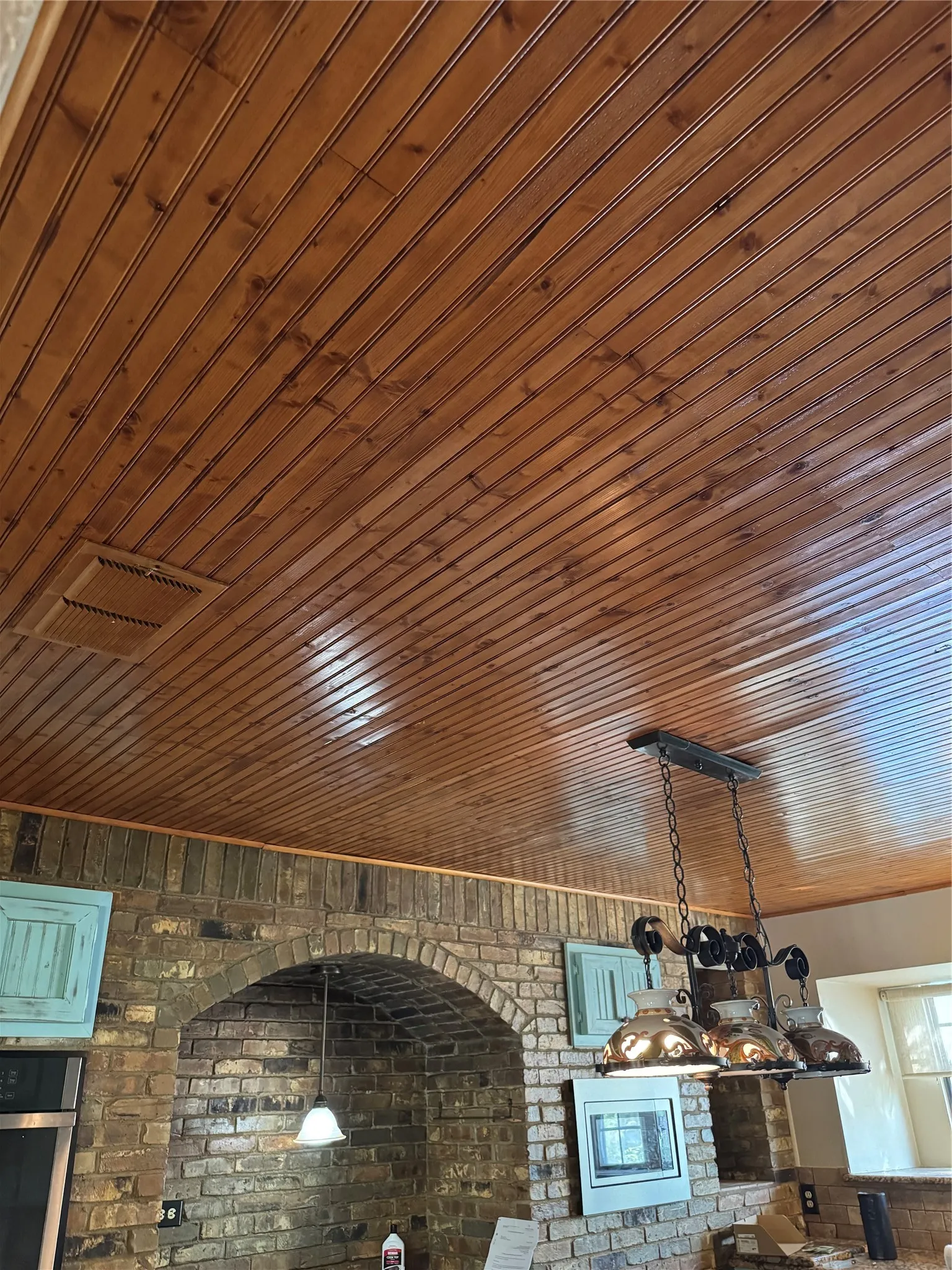 Tongue and Groove Ceiling in Kitchen with brick wall housing the stove and double ovens with microwave. This kitchen was fully remodeled in 2019