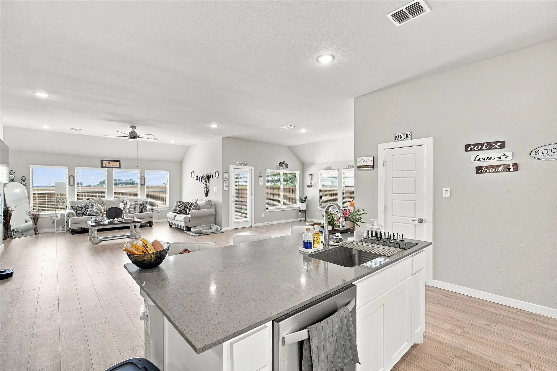Open-concept living space featuring wood-finish flooring, recessed lighting, a vaulted ceiling, and a kitchen island with an undermount sink