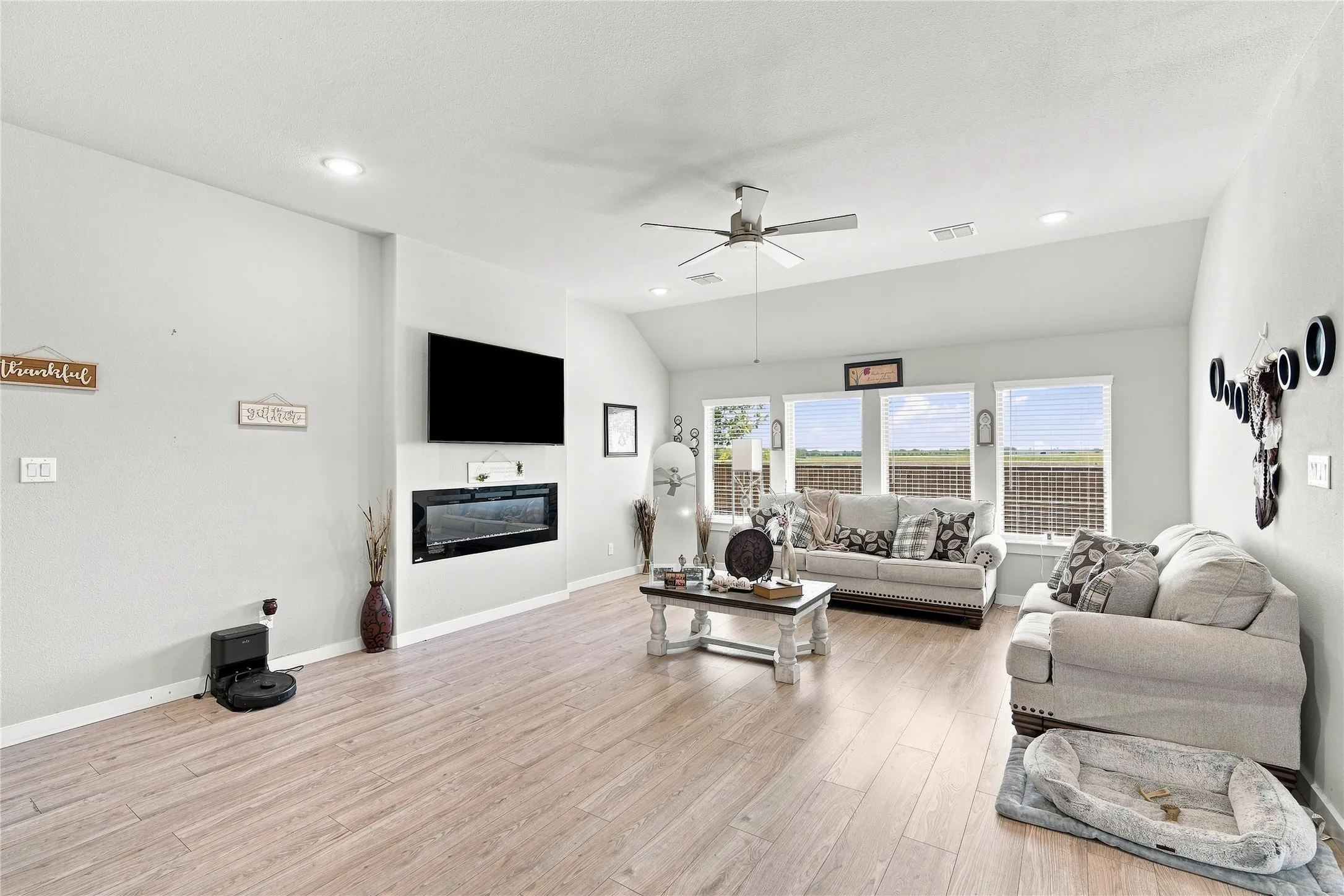 Vaulted ceiling with a ceiling fan, recessed lighting, wood-finish flooring, built-in fireplace, and expansive windows