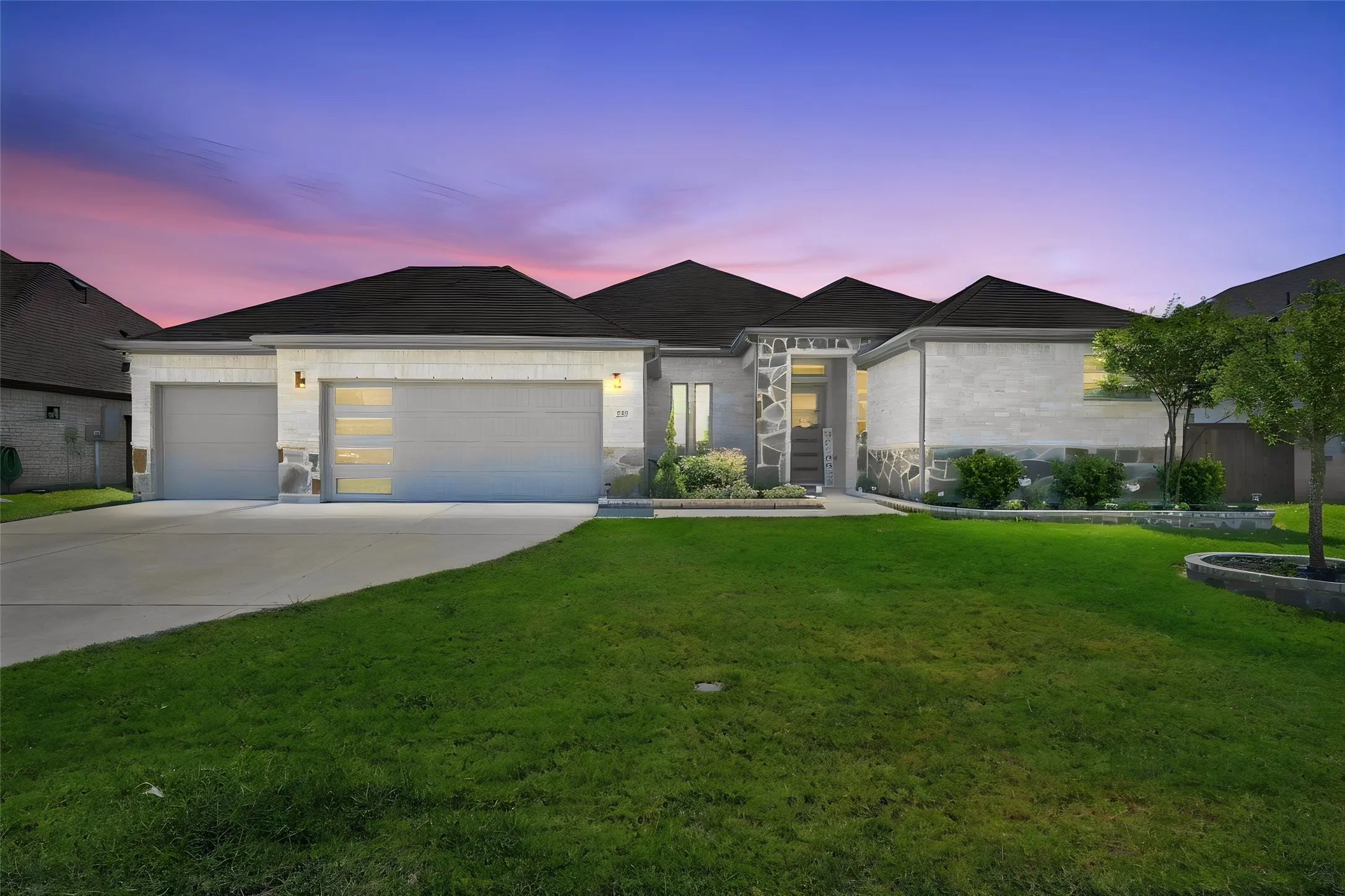 Modern architecture featuring a stone and masonry exterior, two garage bays, concrete driveway, and front landscaping