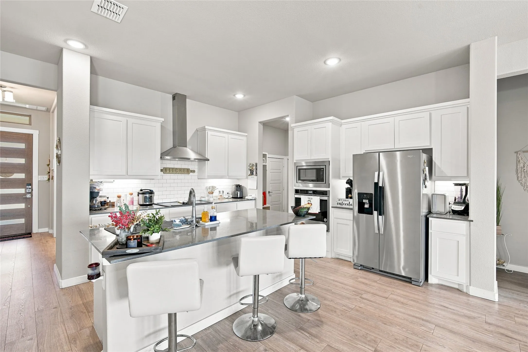 Kitchen featuring stainless steel appliances, wood-finish flooring, recessed lighting, white cabinetry, and an island with bar seating