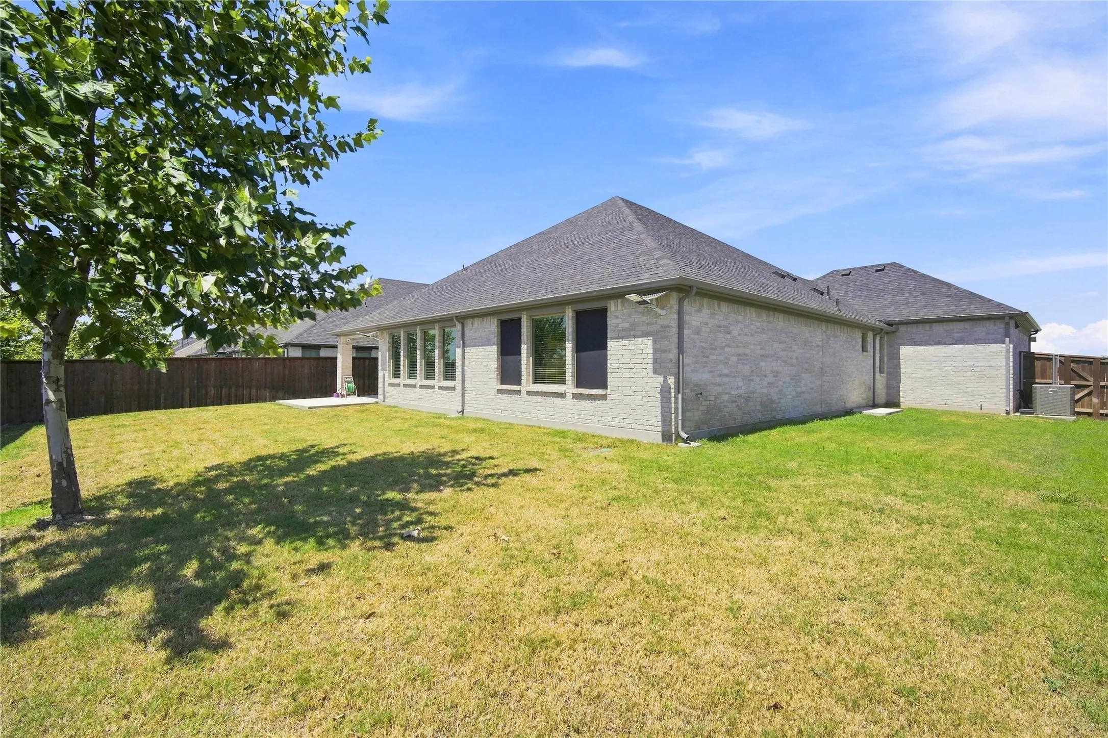 Expansive backyard featuring a manicured lawn, a mature shade tree, a concrete patio, and a privacy fence