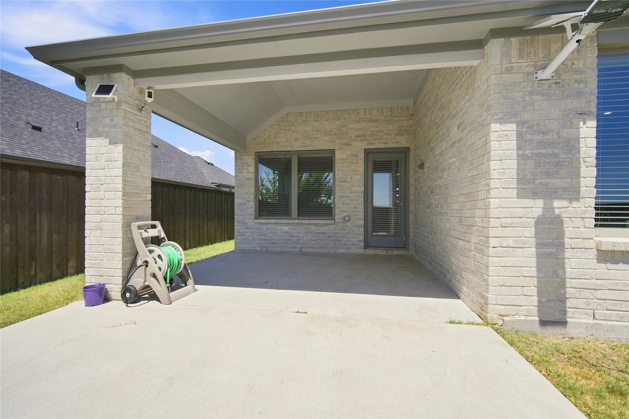 Covered patio with a concrete slab, light-toned brick exterior, and dark-framed windows