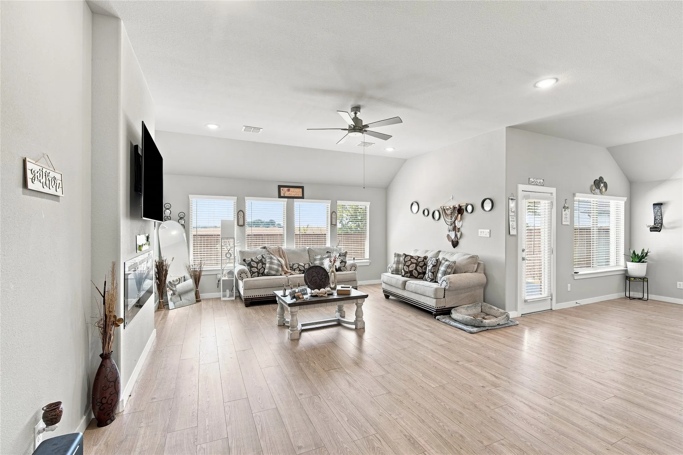 Spacious living area featuring wood-finish flooring, vaulted ceilings, recessed lighting, and multiple windows