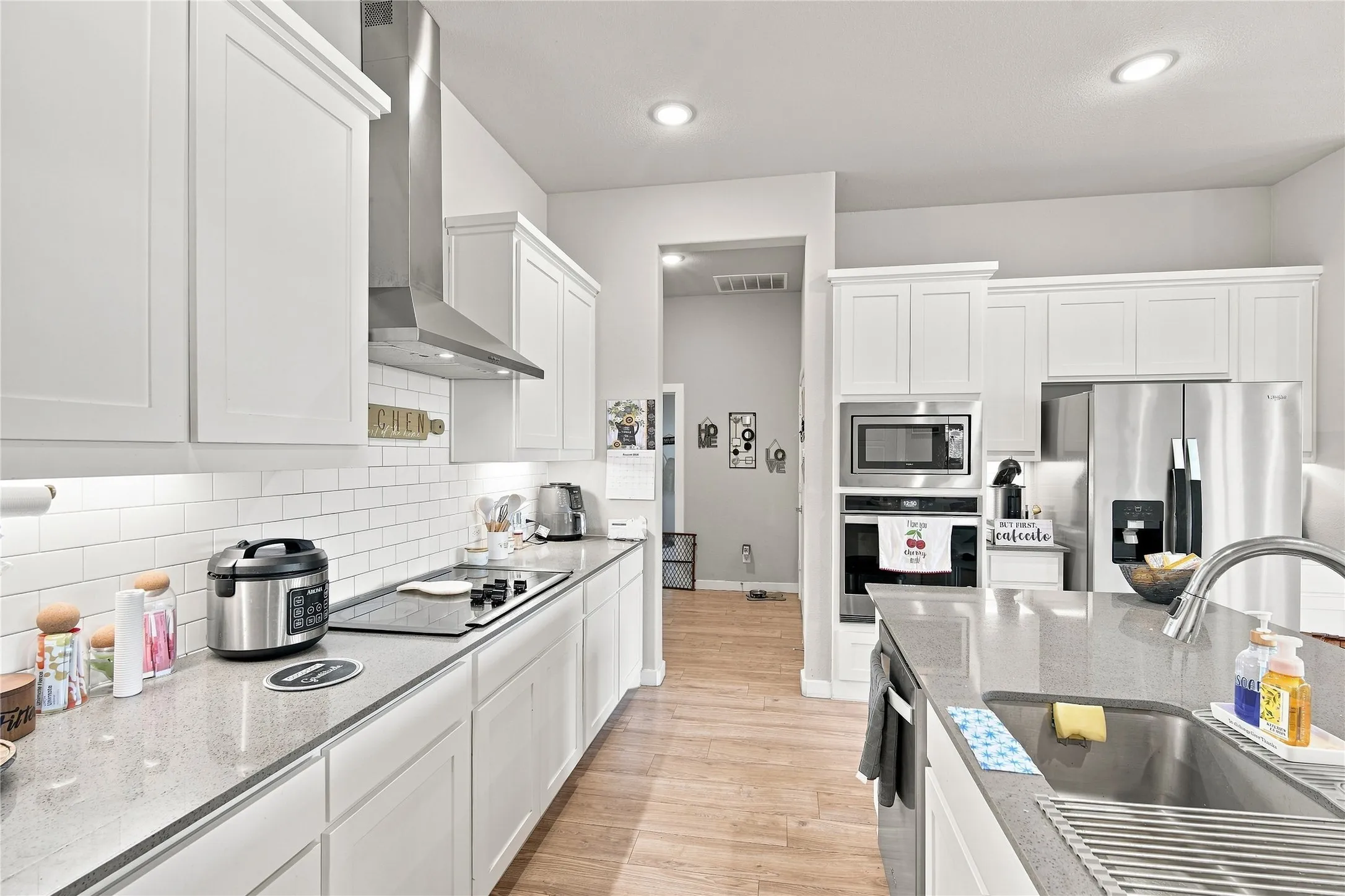 White shaker cabinetry, stainless steel appliances, grey solid surface countertops, subway tile backsplash, and wood-finish flooring