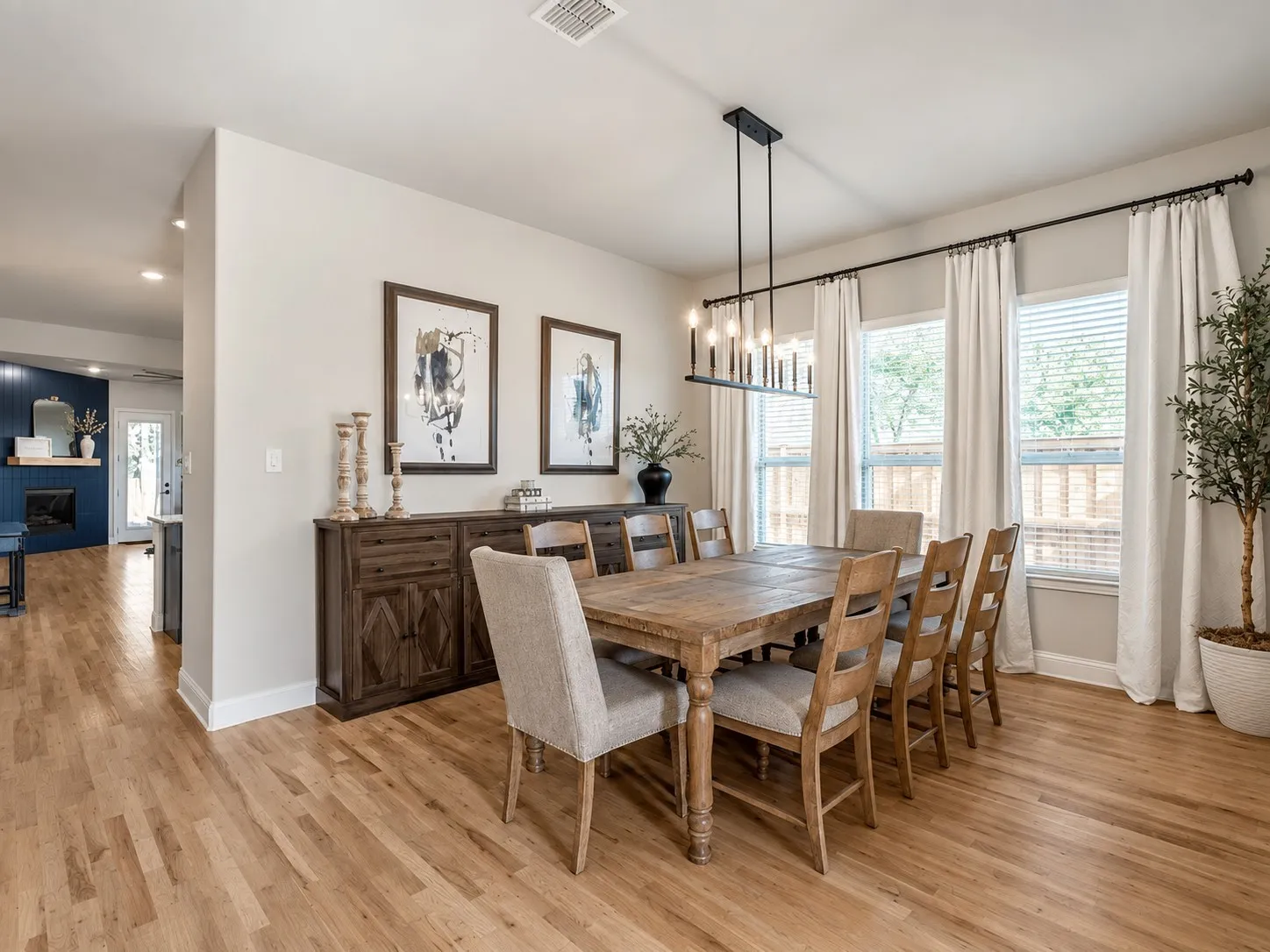 Hardwood flooring extends throughout, complemented by a modern linear chandelier and multiple windows