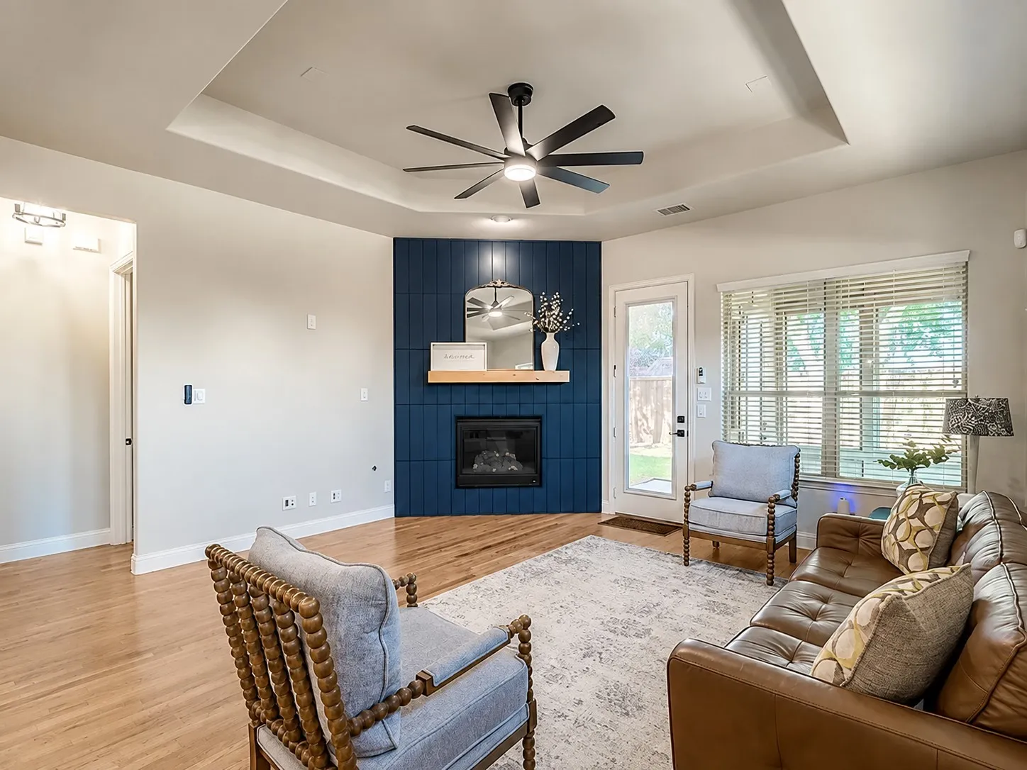 Tray ceiling with a modern ceiling fan, wood-finish flooring, and a corner fireplace with a blue-tiled accent wall and mantel