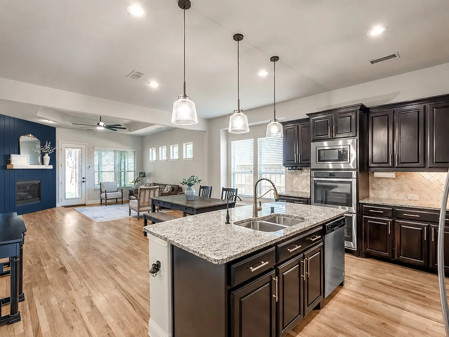 Open-concept living area with wood-finish flooring, a kitchen island with granite countertops, dark wood cabinetry, and stainless steel built-in appliances