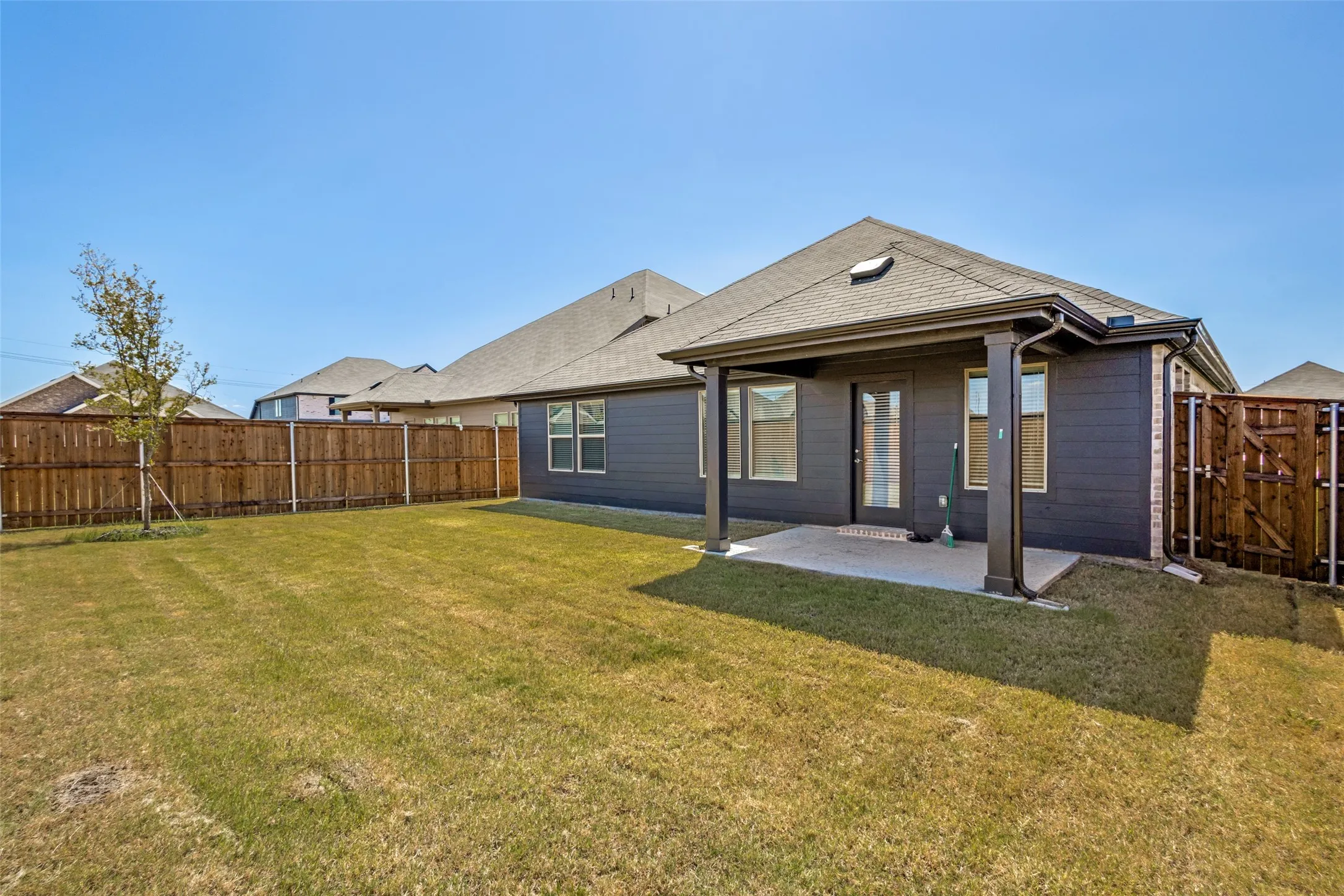 Expansive backyard featuring a covered patio, privacy fencing, and a mature tree