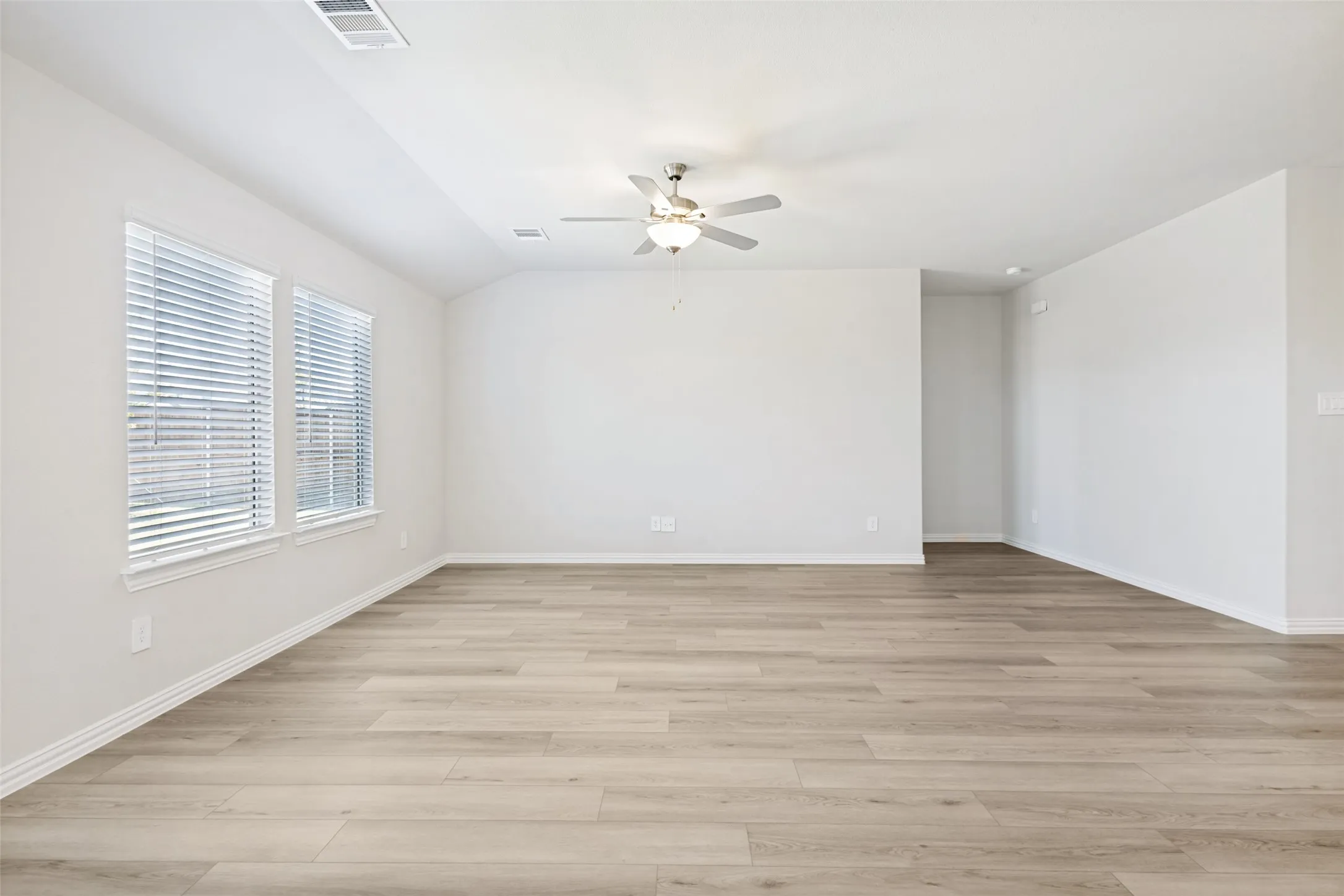 Spacious interior with wood-finish flooring, multiple windows with blinds, and an overhead ceiling fan