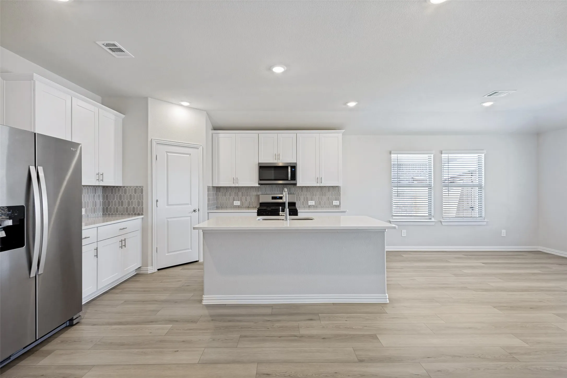 Open-concept living space with recessed lighting, wood-finish flooring, and two windows with blinds