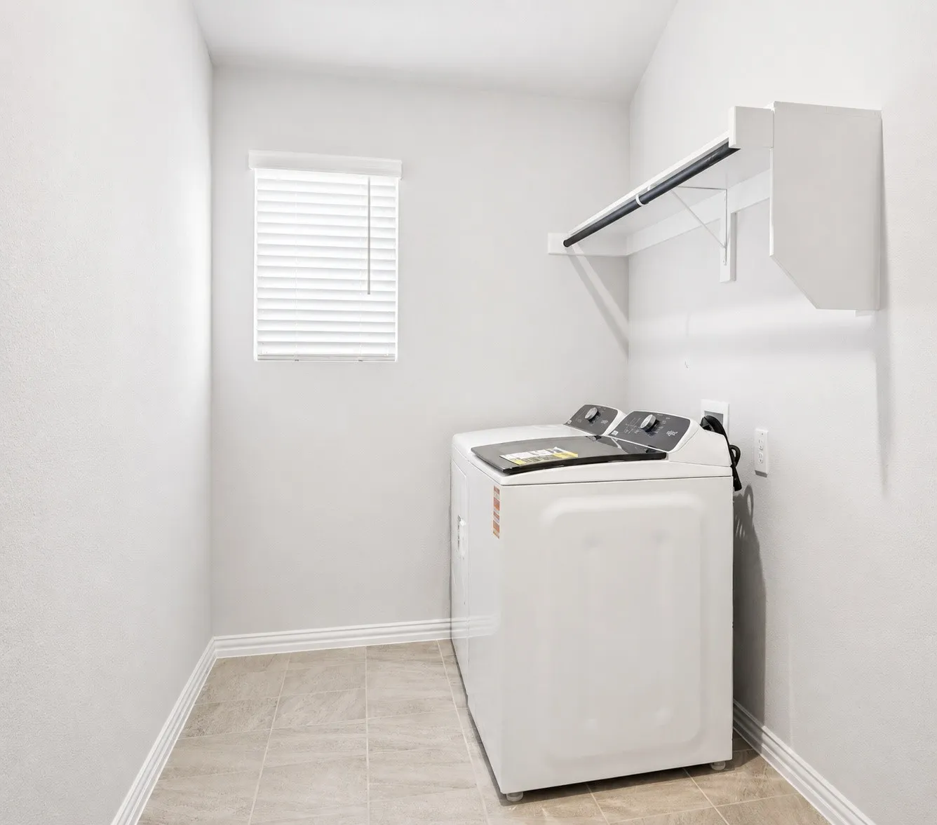 Over-size Laundry room featuring neutral wall paint, tiled flooring, a window with blinds, and a built-in hanging rod with shelving