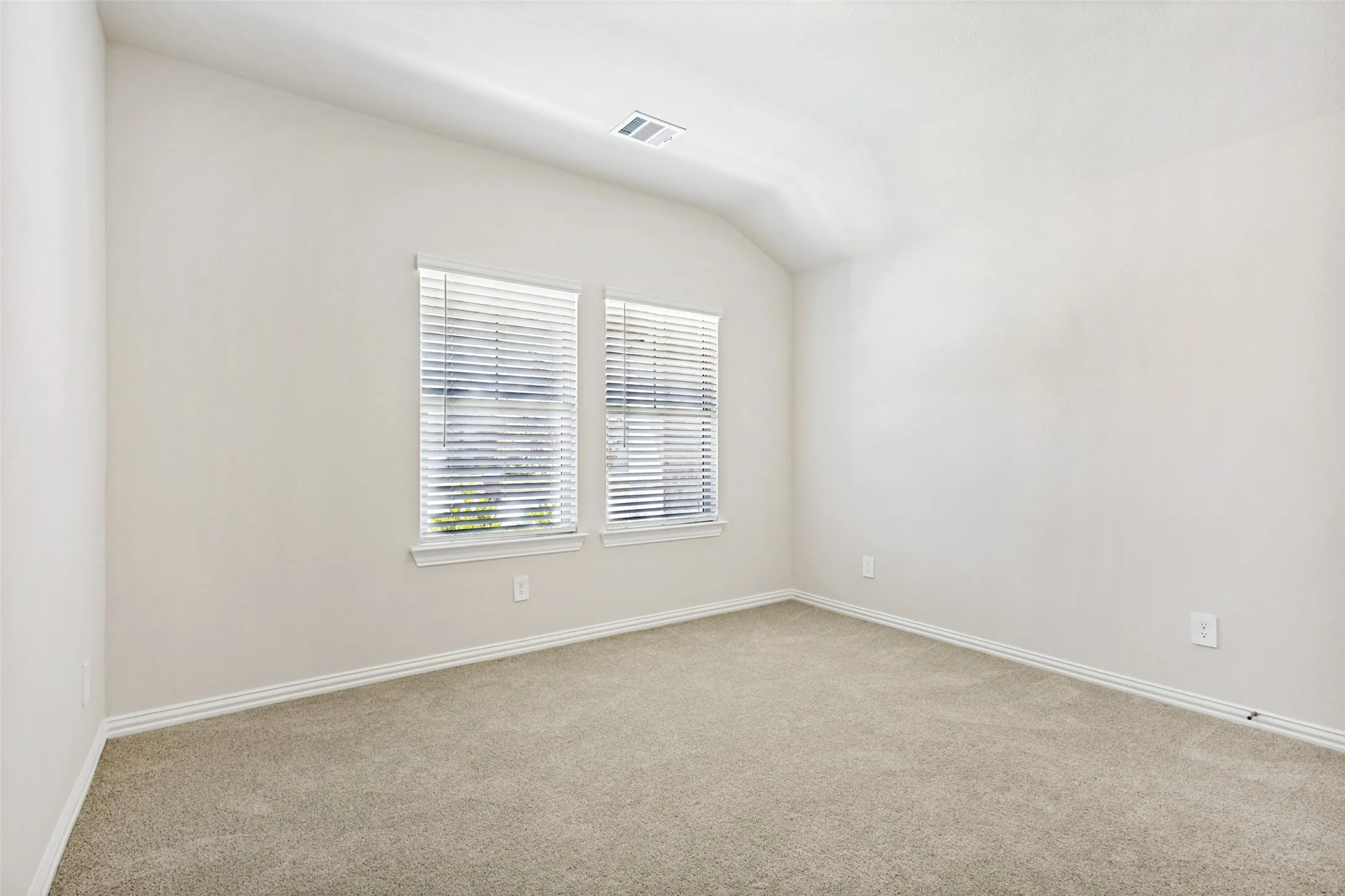 Vaulted ceiling, two windows with blinds, light-toned carpet, and neutral wall color