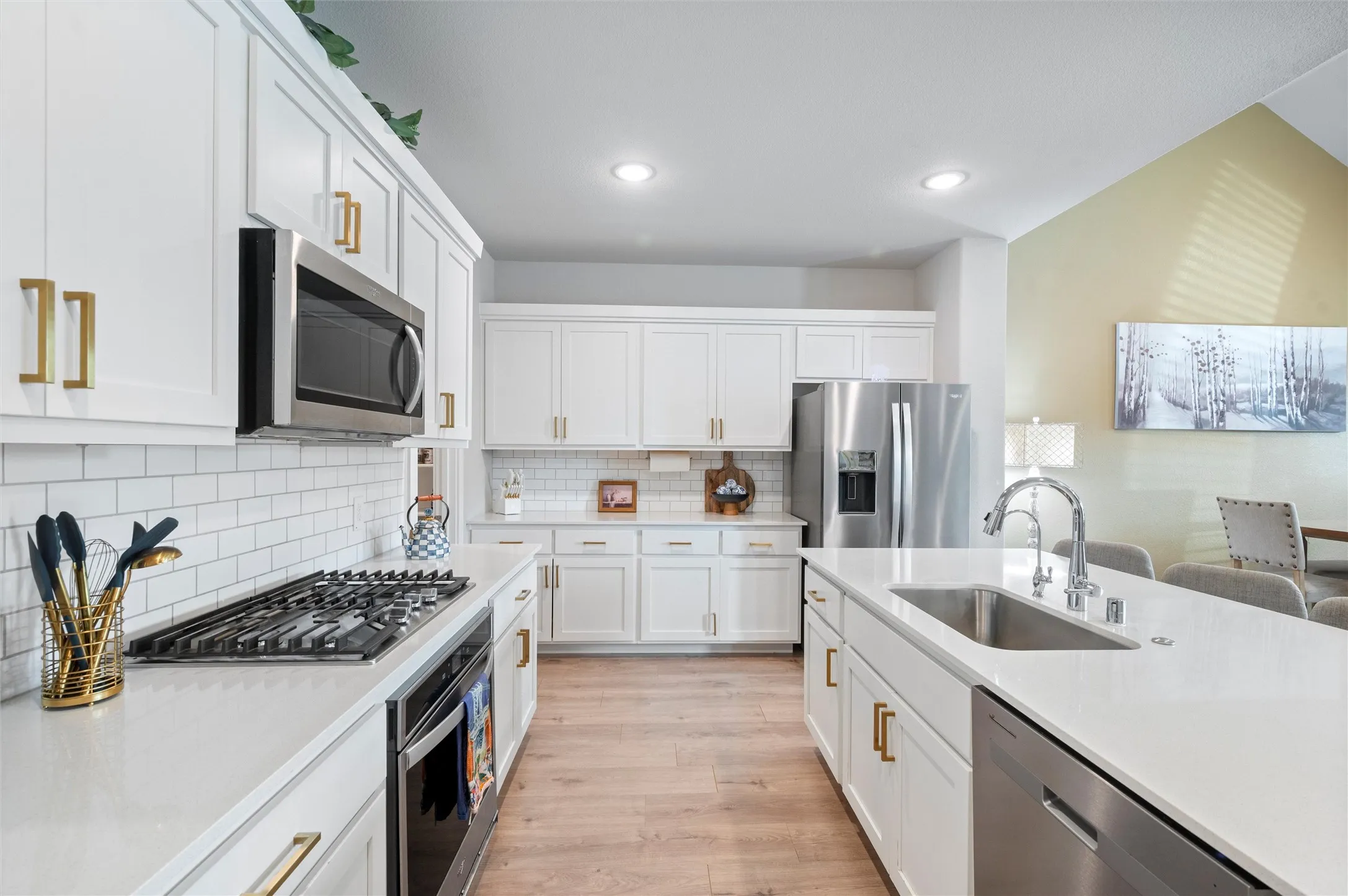 Kitchen featuring white cabinetry, stainless steel appliances, a center island with an undermount sink, and wood-finish flooring