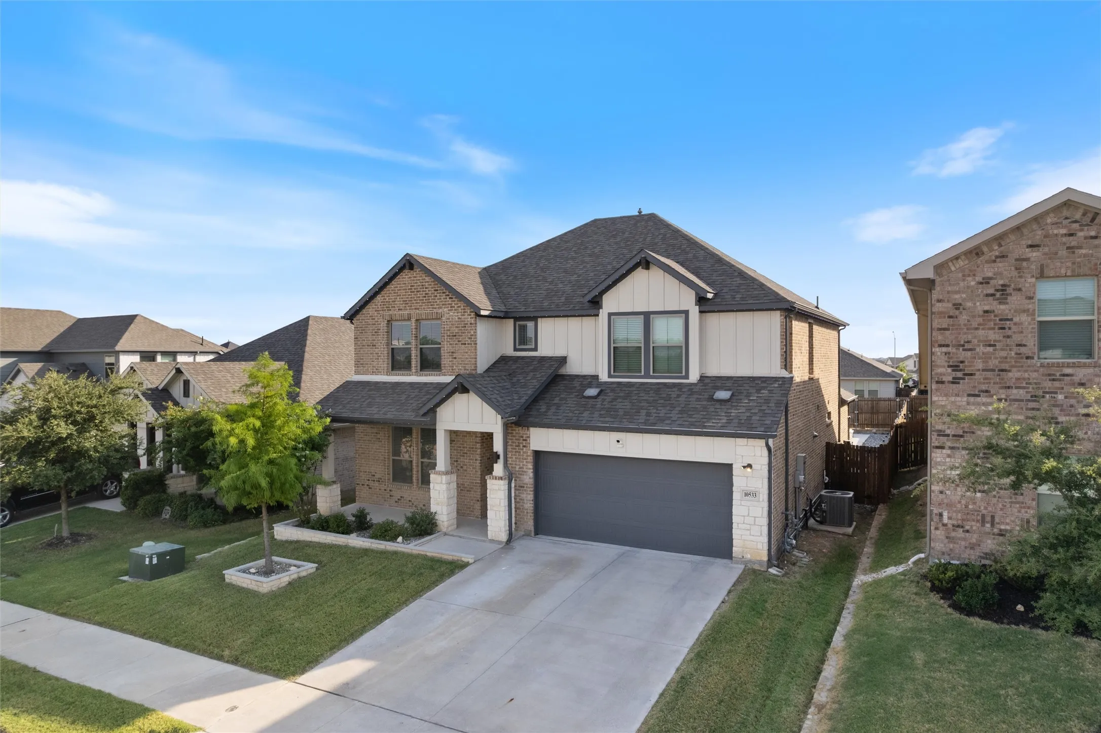 Two-story residence featuring a brick and siding exterior, an attached garage, a paved driveway, a landscaped front yard with mature trees, and a covered front porch