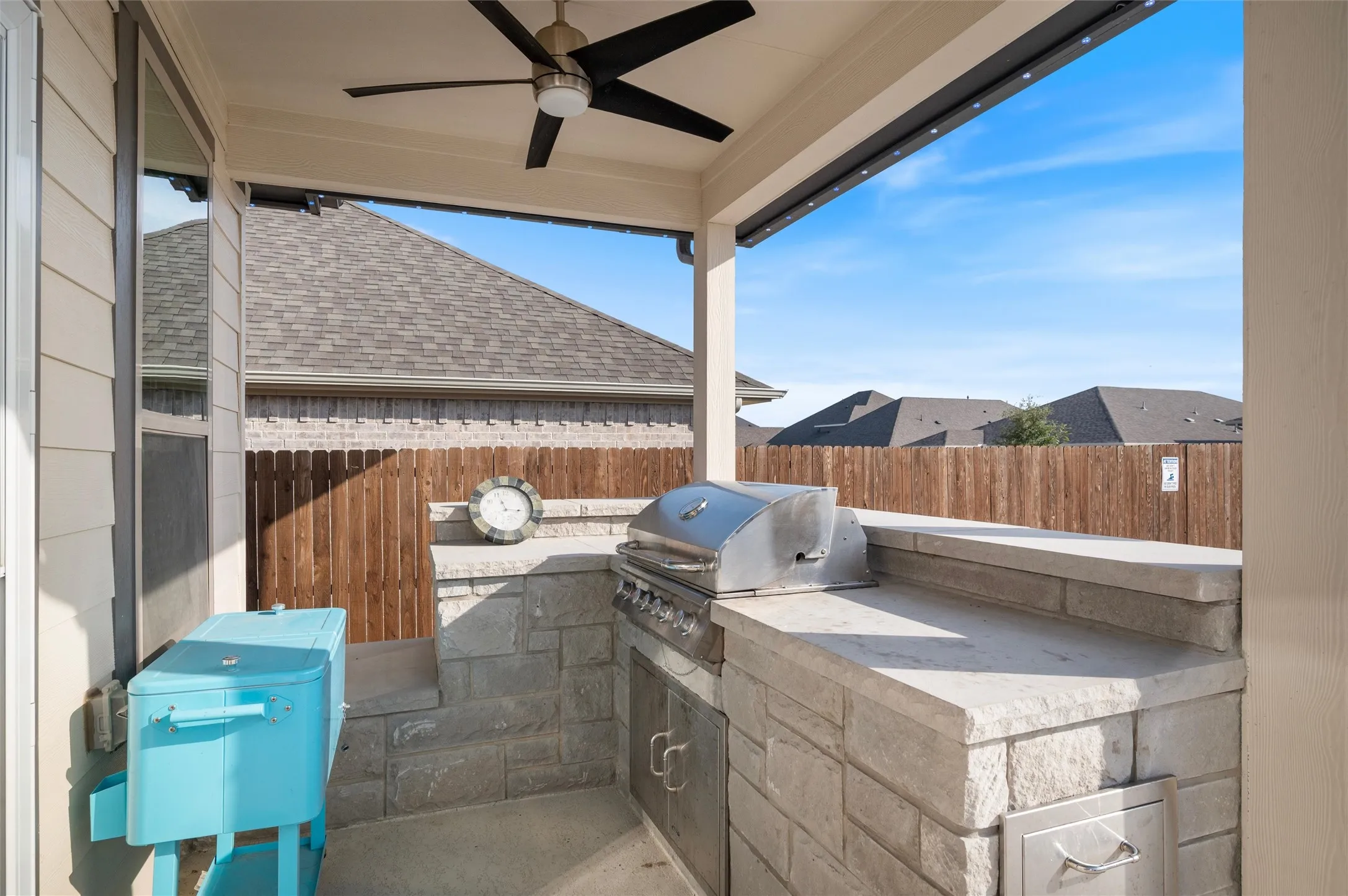 Covered patio with a built-in outdoor kitchen, stainless steel grill, and stone veneer surround
