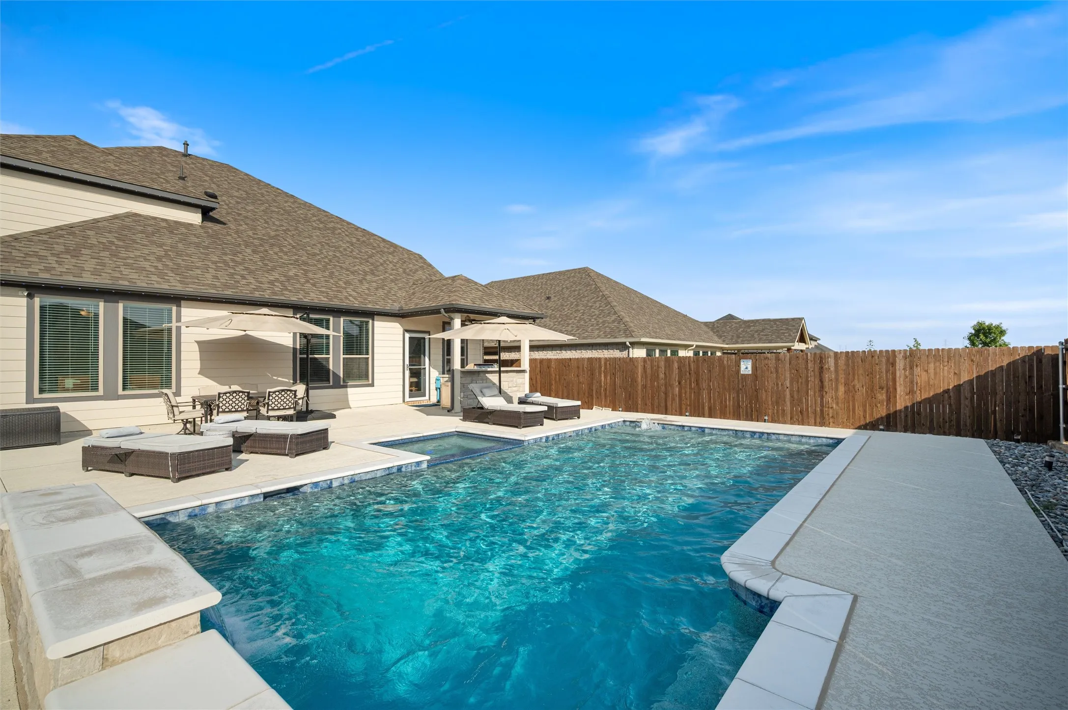 Expansive outdoor space featuring a rectangular pool, integrated spa, surrounding concrete patio, and a wood privacy fence