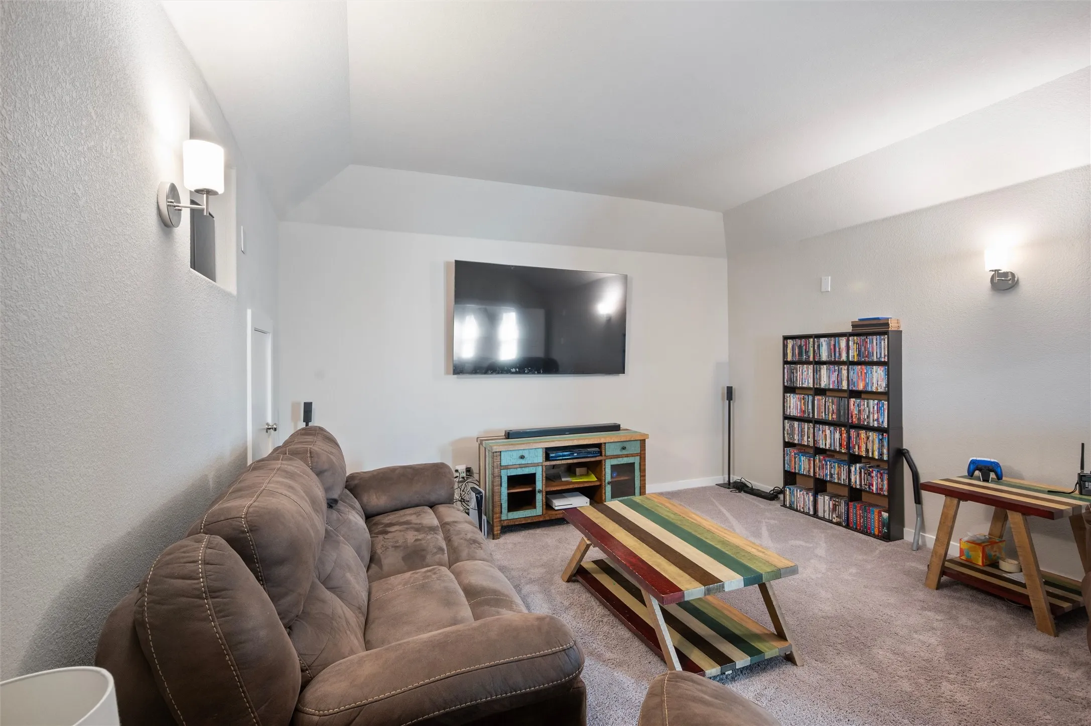 Vaulted ceiling, wall-mounted sconce lighting, and soft carpet flooring