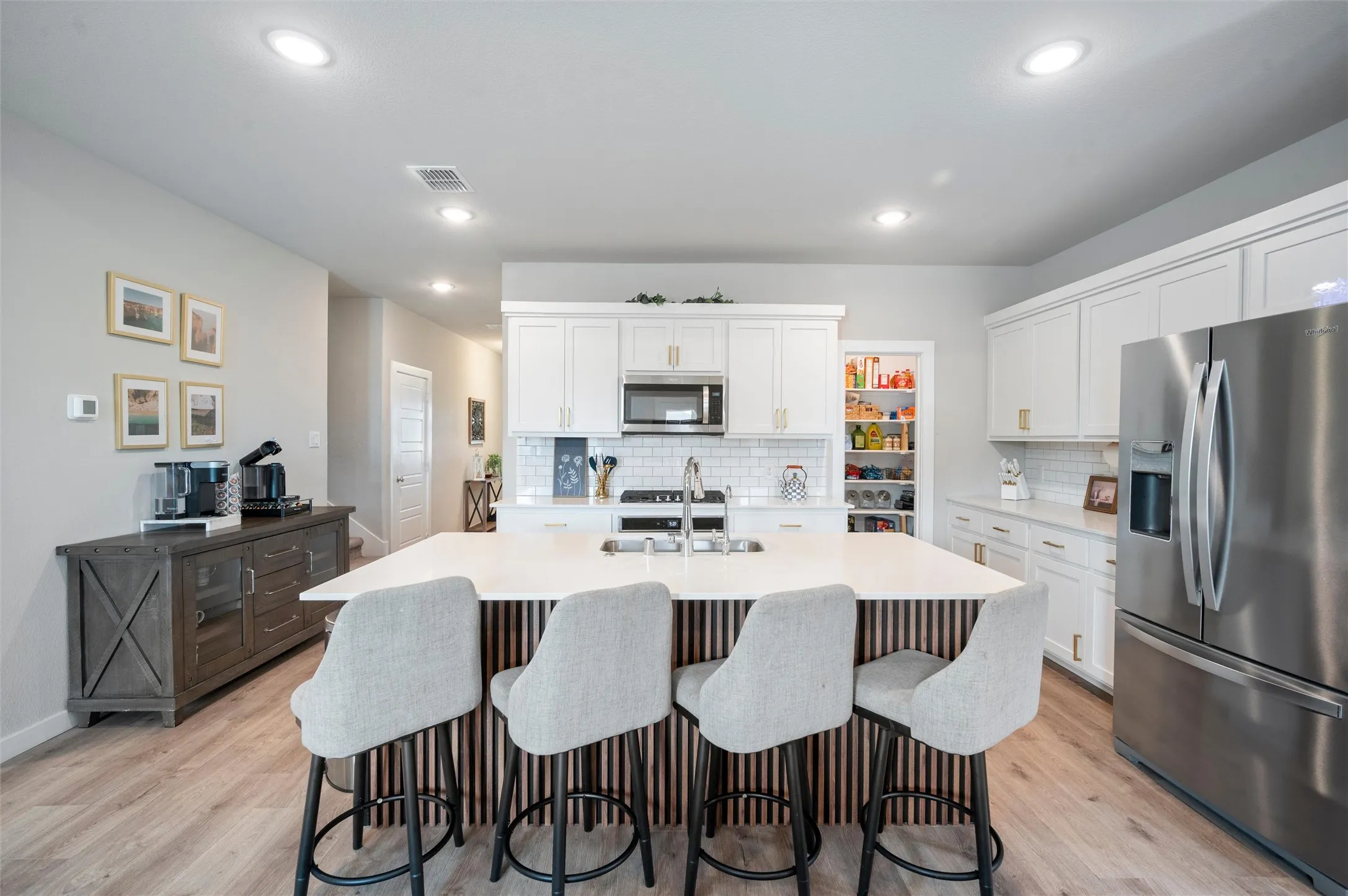 Kitchen featuring a large island with white countertop, subway tile backsplash, white cabinetry with gold-finish hardware, stainless steel appliances, and wood-finish flooring