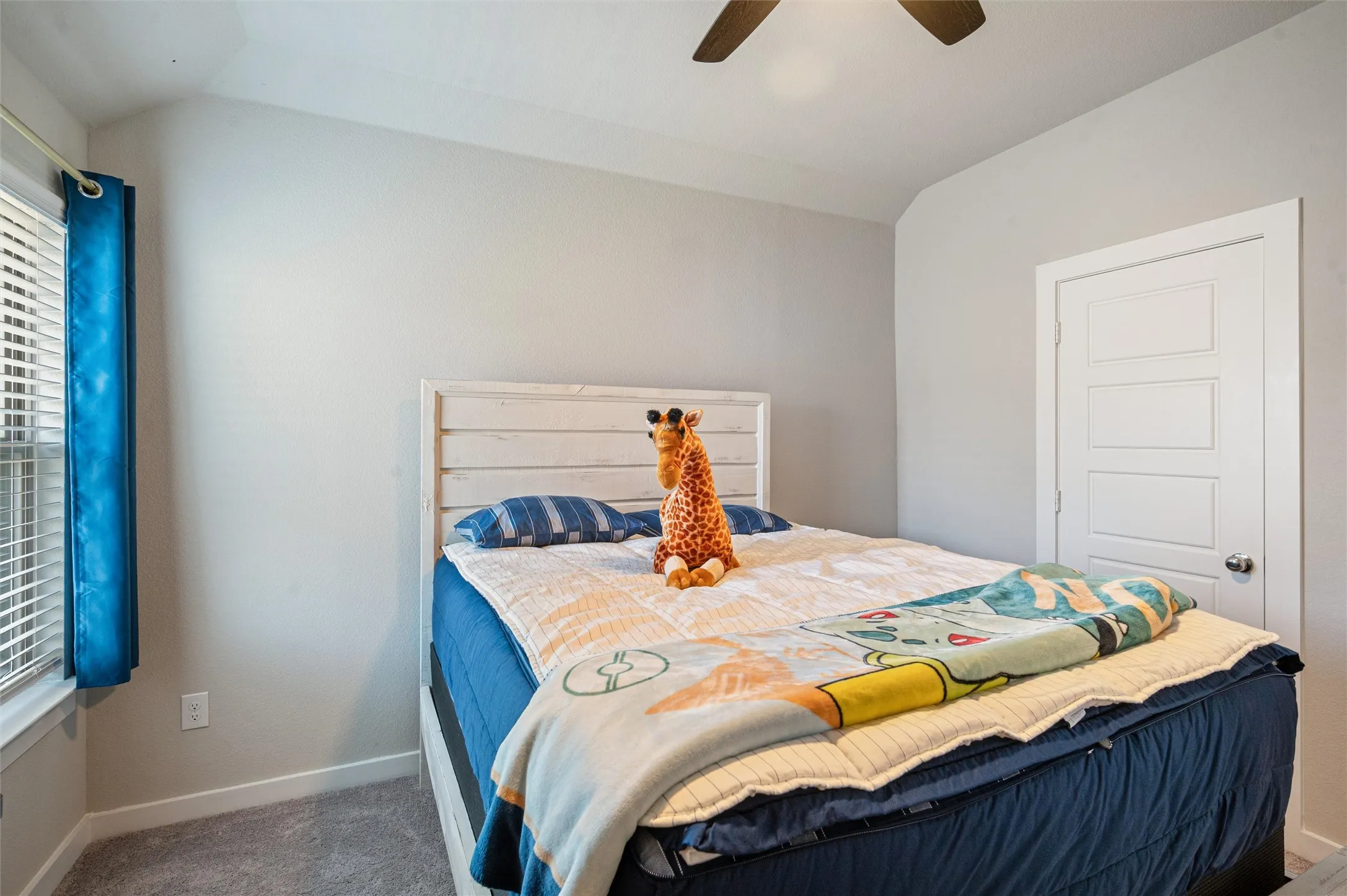 Carpeted flooring, vaulted ceiling, ceiling fan, window with blinds, and a paneled door