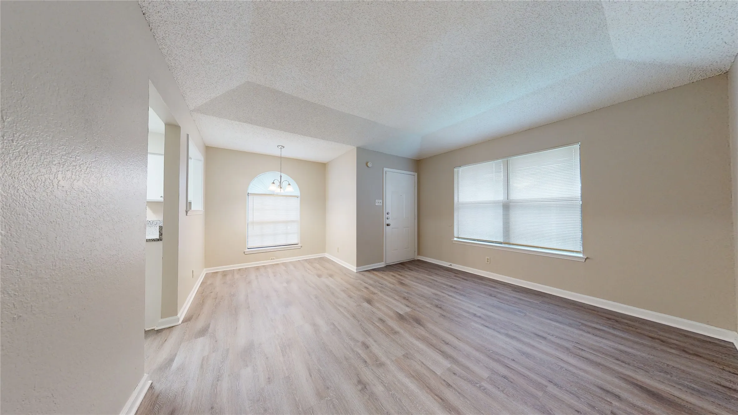 Wood-finish flooring, vaulted ceiling, and an arched window with an attached pendant light