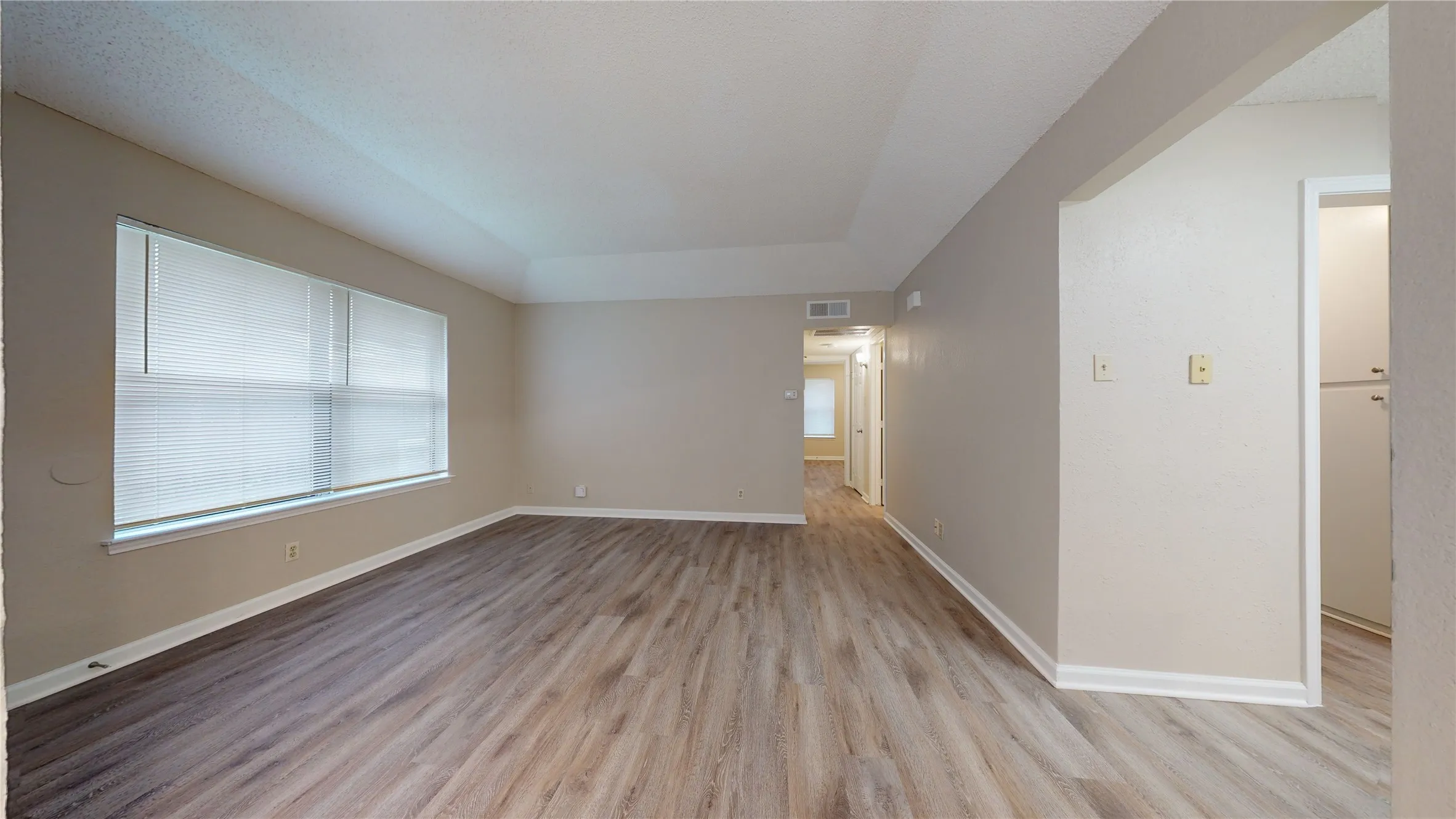 Spacious room featuring wood-finish flooring, light-toned walls, and a large window with blinds