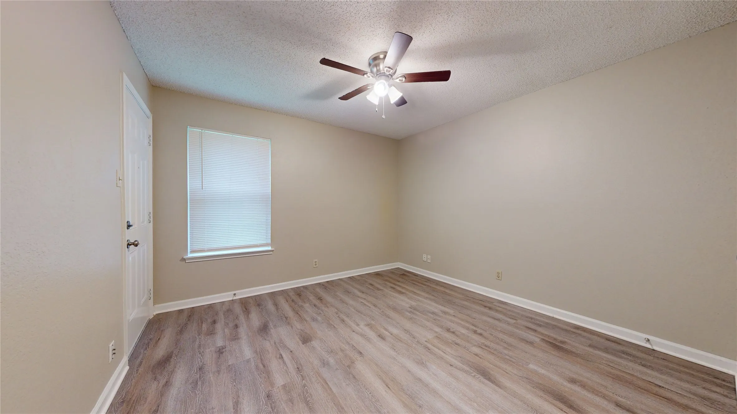 Spacious room featuring wood-finish flooring, a ceiling fan with integrated lighting, a window with blinds, and neutral wall tones