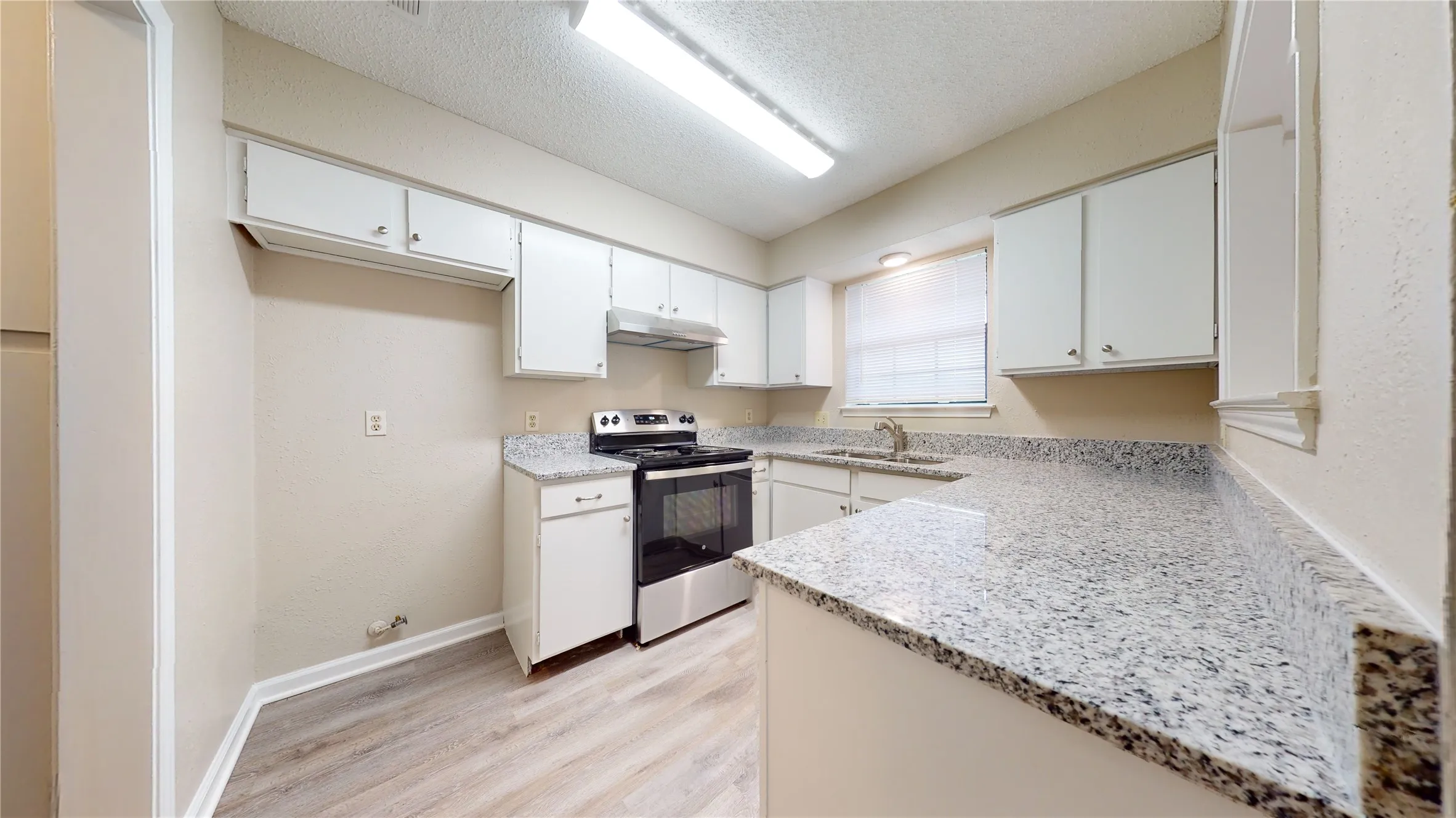 White cabinetry with chrome hardware, stone-finish countertops, stainless steel range, and wood-finish flooring