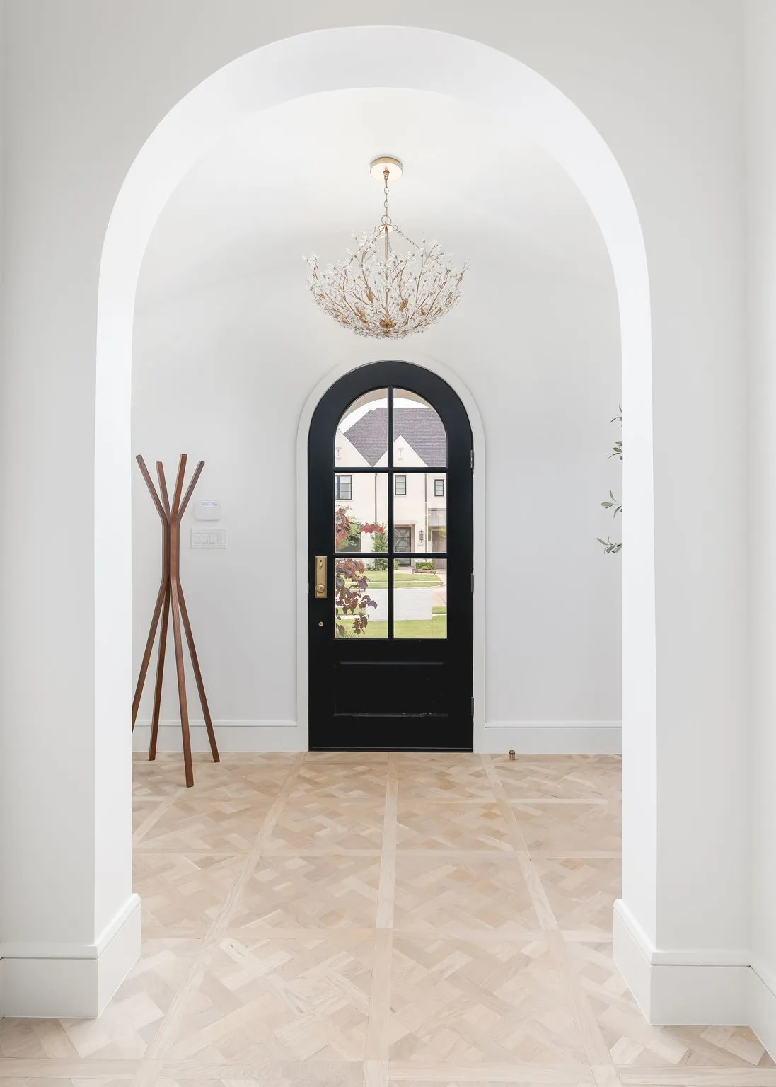 Arched entryway featuring a black arched door with glass panes, a decorative chandelier, and light wood-finish flooring with a geometric pattern