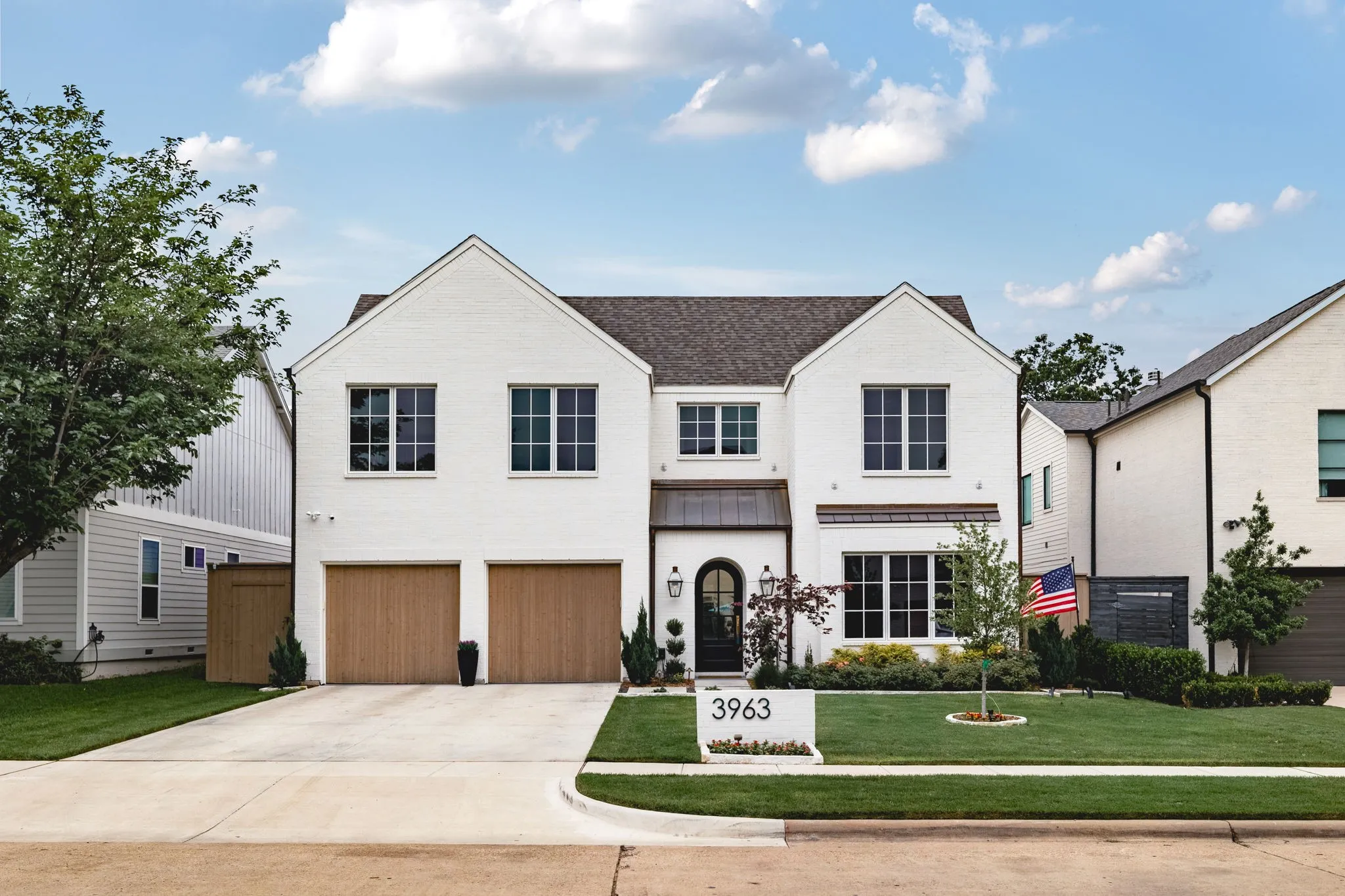 White brick exterior with a dark shingle roof, two wood-finish garage doors, and a concrete driveway