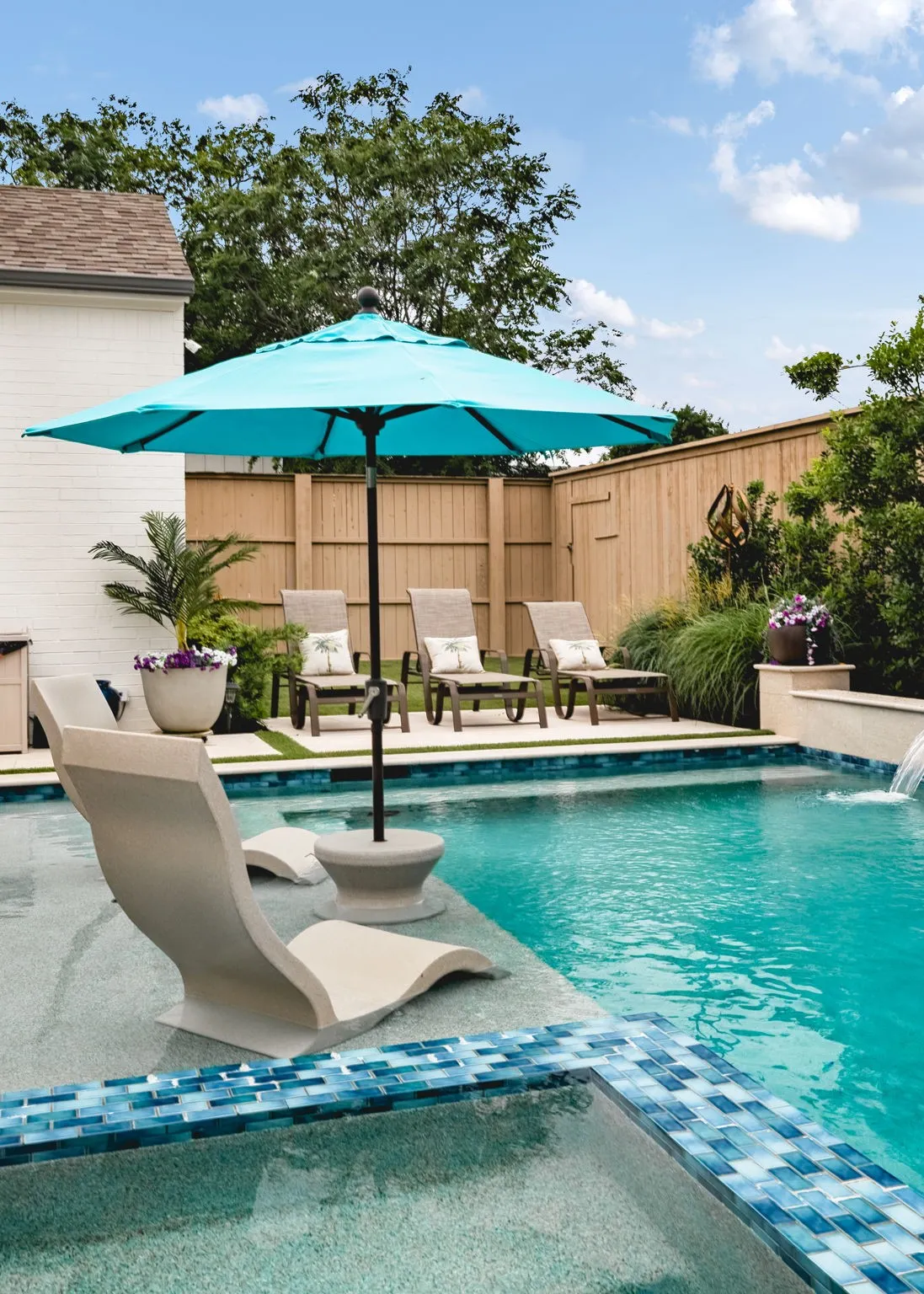 Integrated swimming pool with blue mosaic tile accents and a waterfall feature, surrounded by artificial turf and a privacy fence