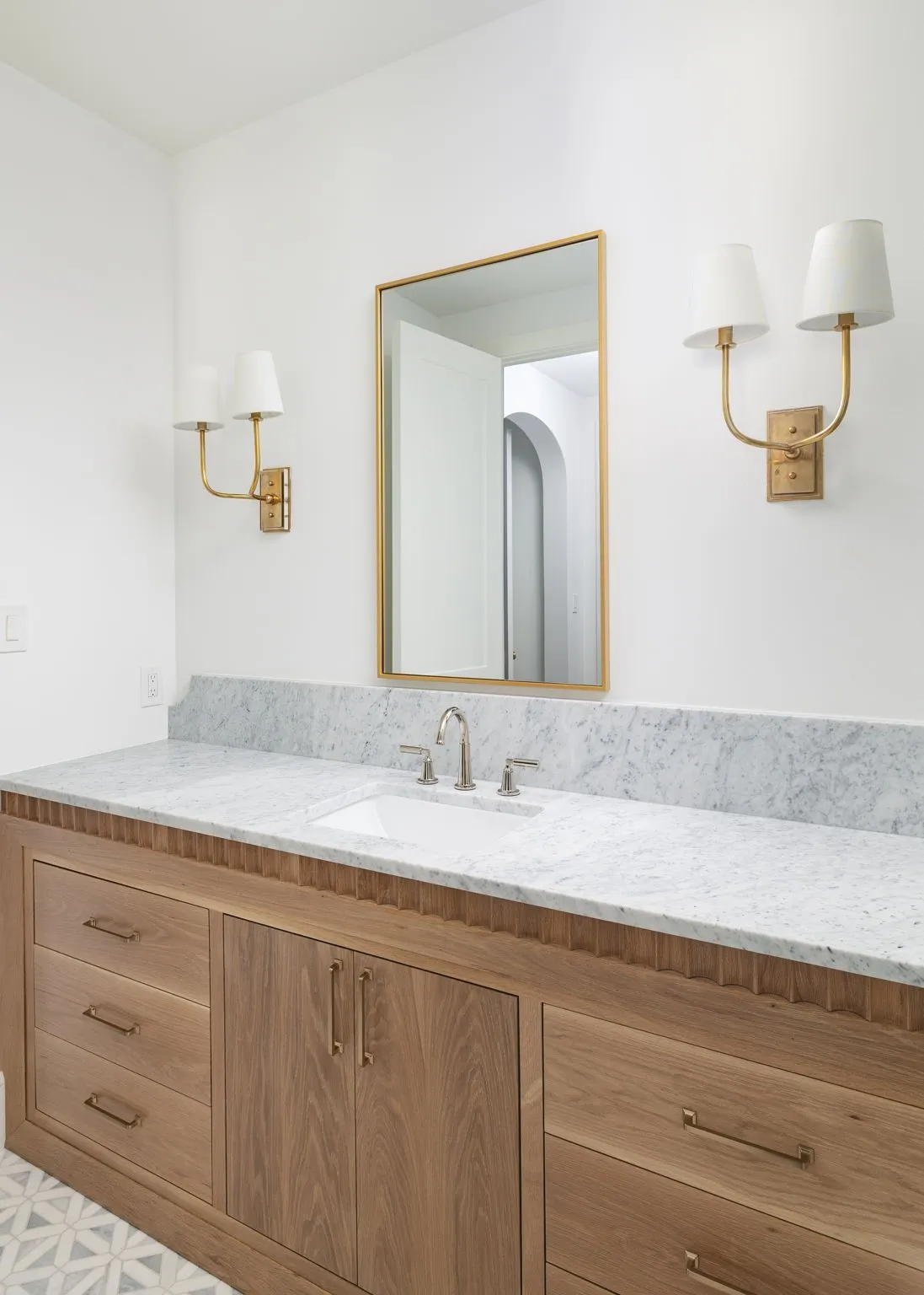 Custom wood vanity with brass hardware, undermount sink, stone countertop, and decorative wall sconces