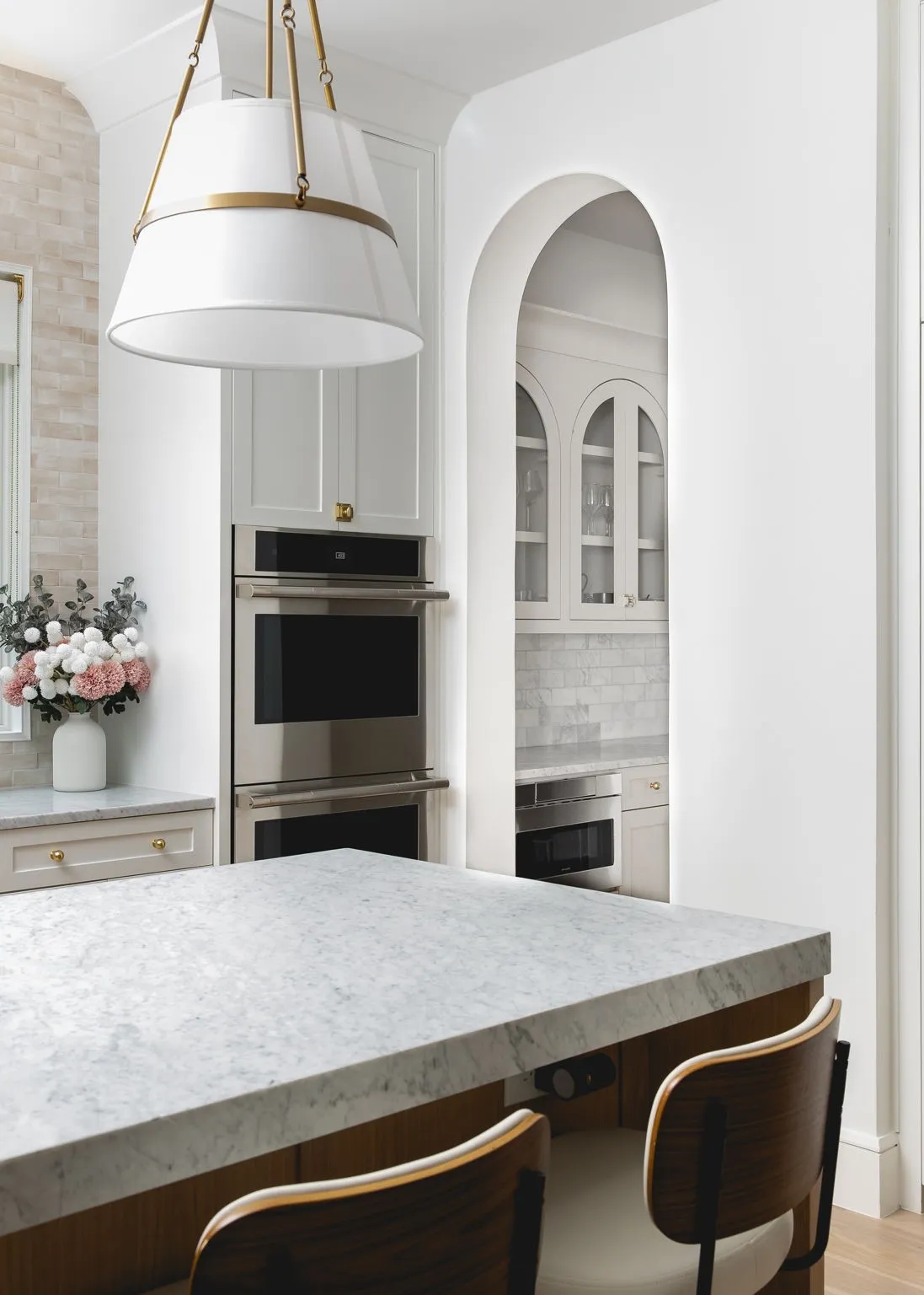 Kitchen featuring a light-toned stone countertop, integrated stainless steel double ovens, and a decorative pendant light