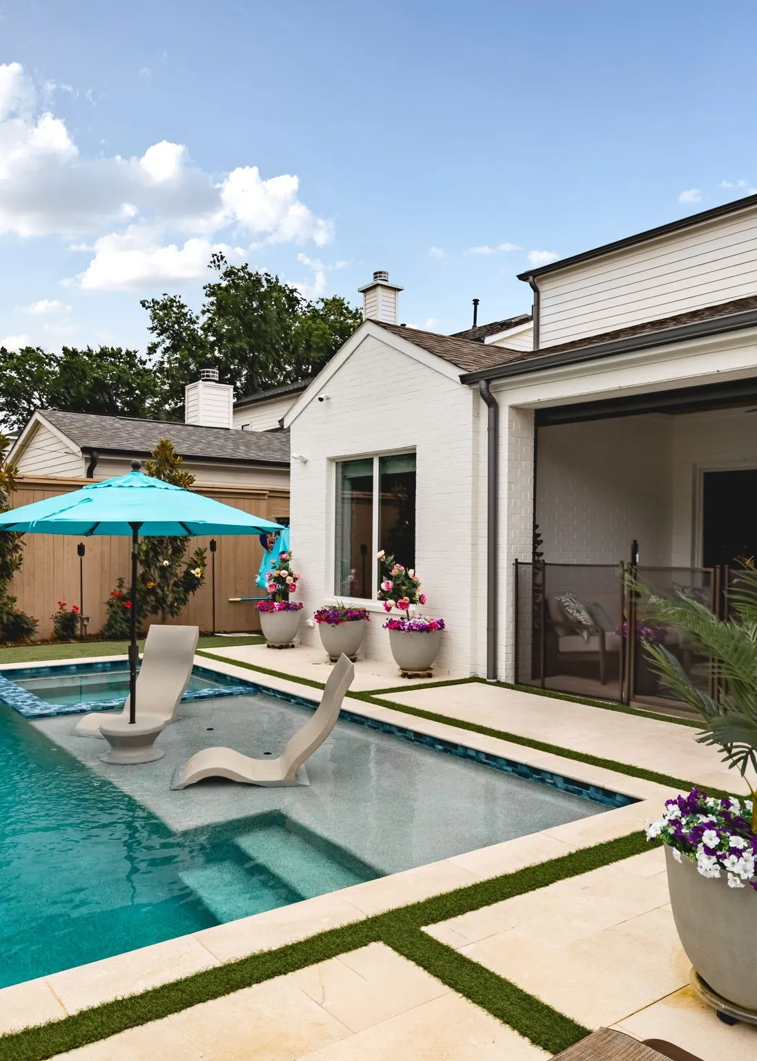 Pool with integrated lounge area, surrounding stone patio with artificial turf accents, and white brick exterior