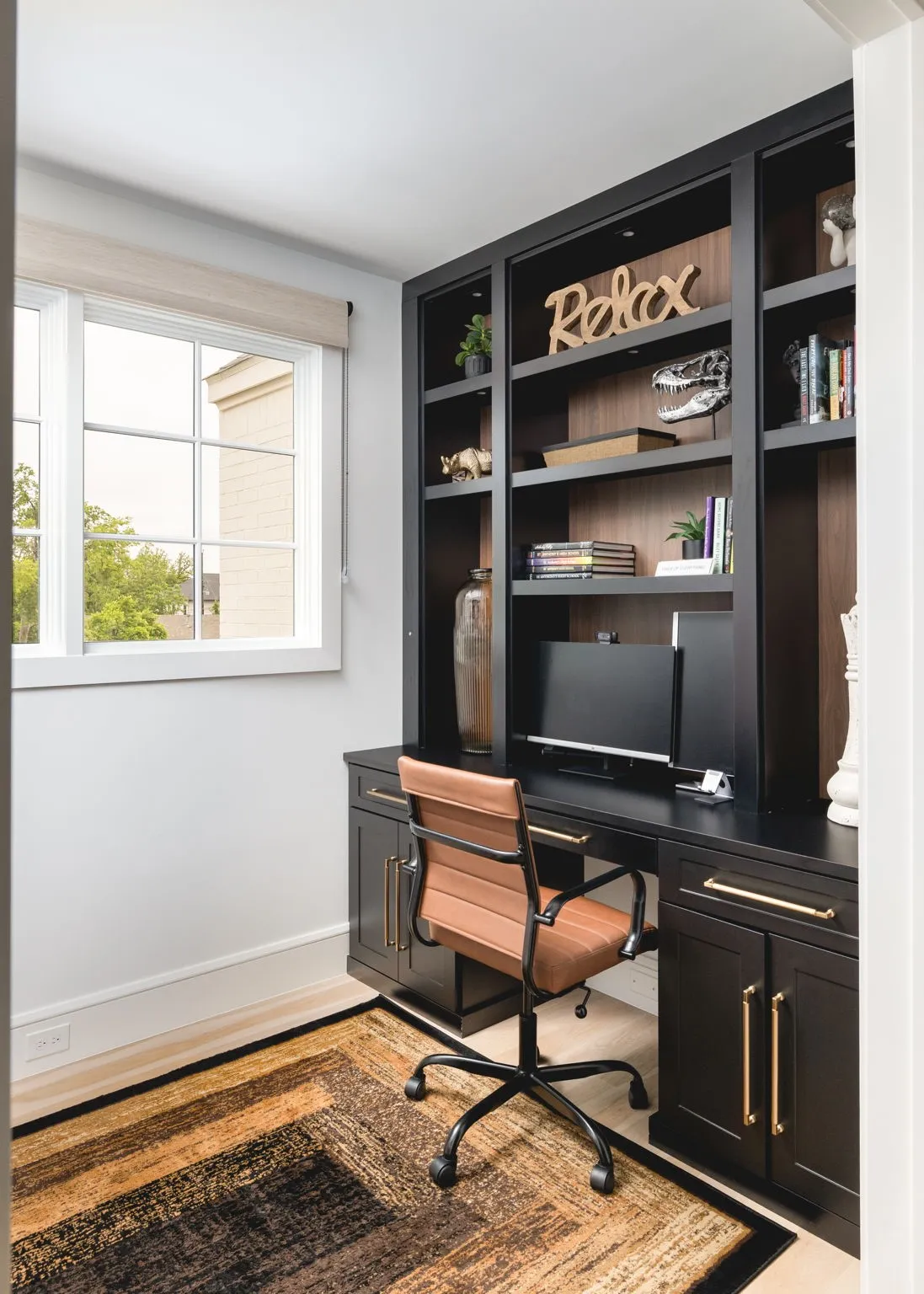 Built-in black cabinetry with gold-finish hardware, integrated desk space, upper shelving with recessed lighting, and wood-finish flooring