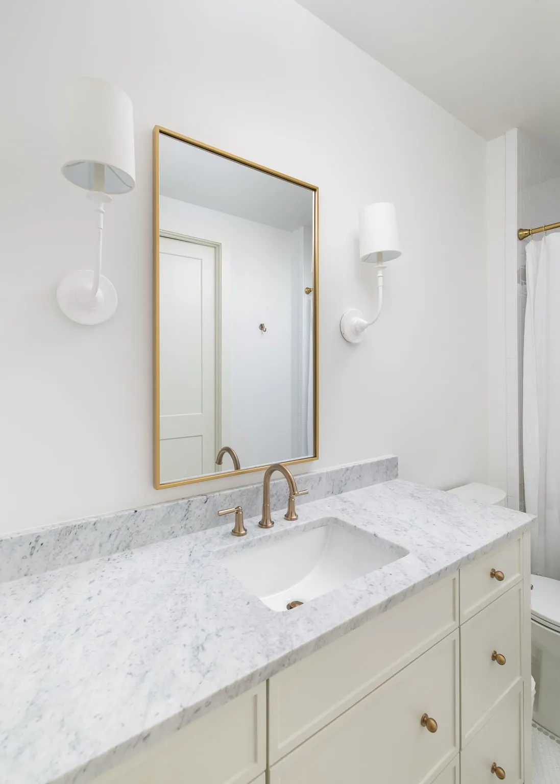 White vanity with integrated sink, stone countertop, gold-framed mirror, and brass-finish fixtures
