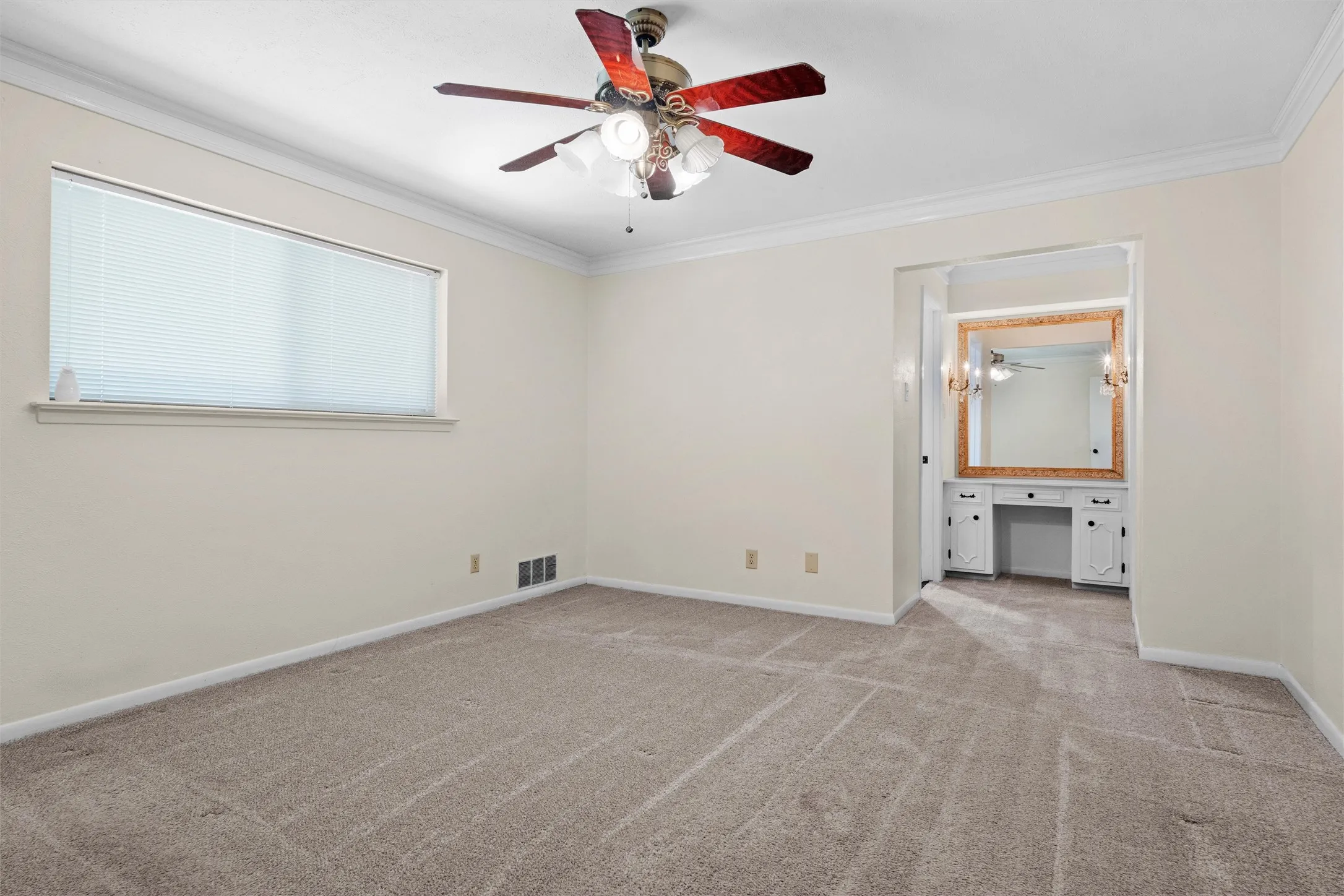Cream-colored walls with crown molding, a window with blinds, a ceiling fan with light fixture, and a built-in vanity with a mirror and sconce lighting