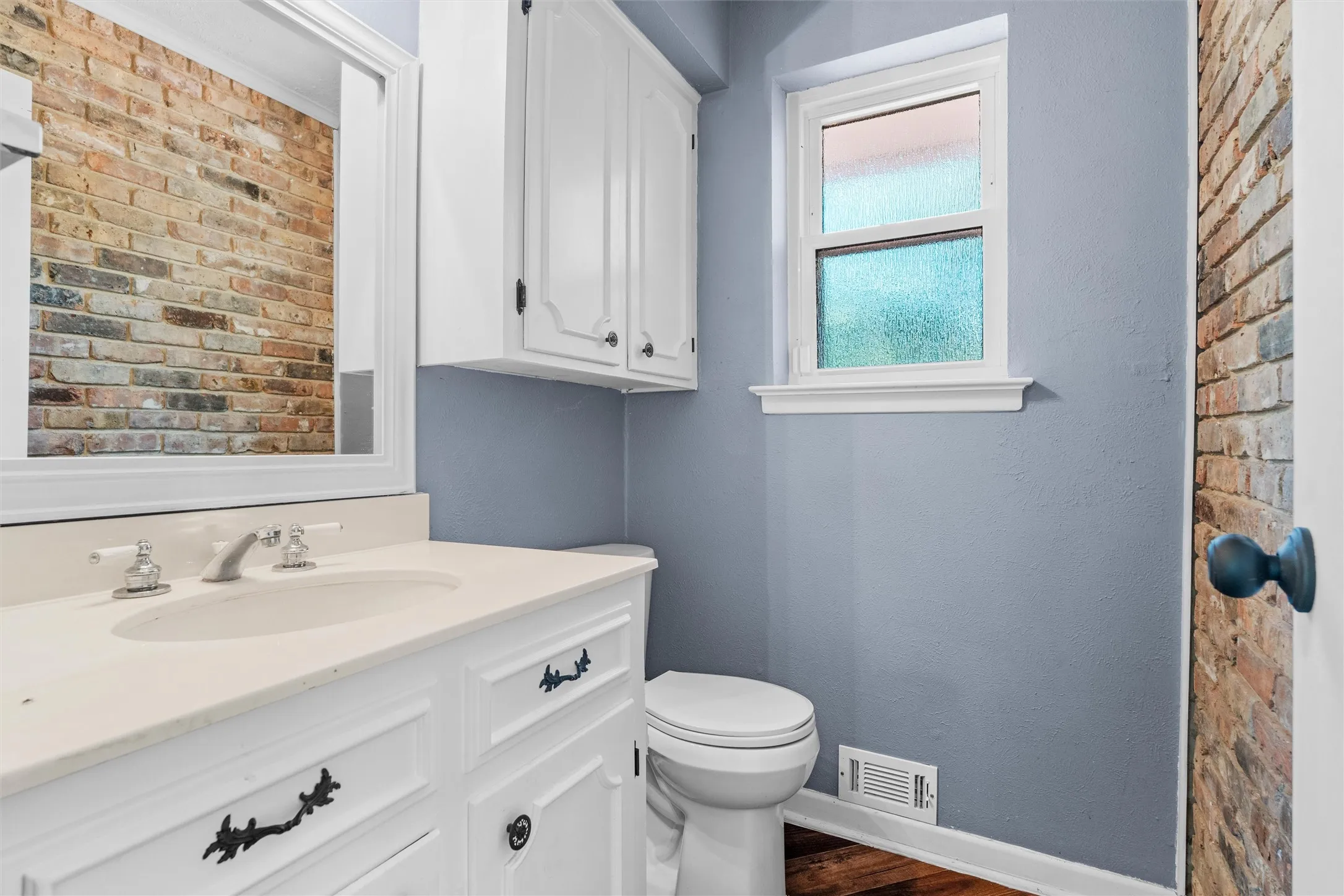 White vanity with an integrated sink and brushed nickel faucet, wall-mounted storage cabinetry, and a window with frosted glass