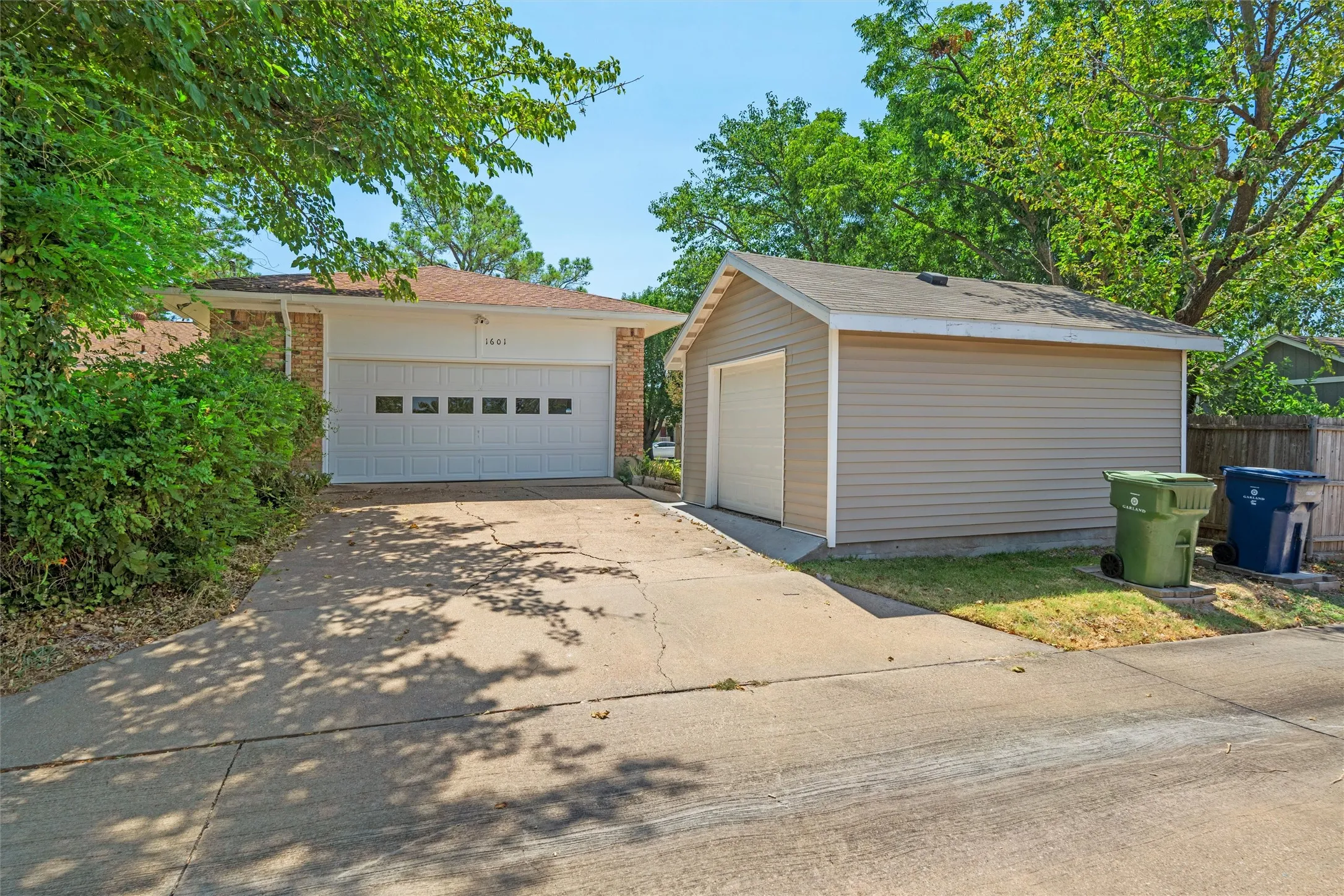 Brick facade, attached garage with panel windows, detached garage, and mature landscaping
