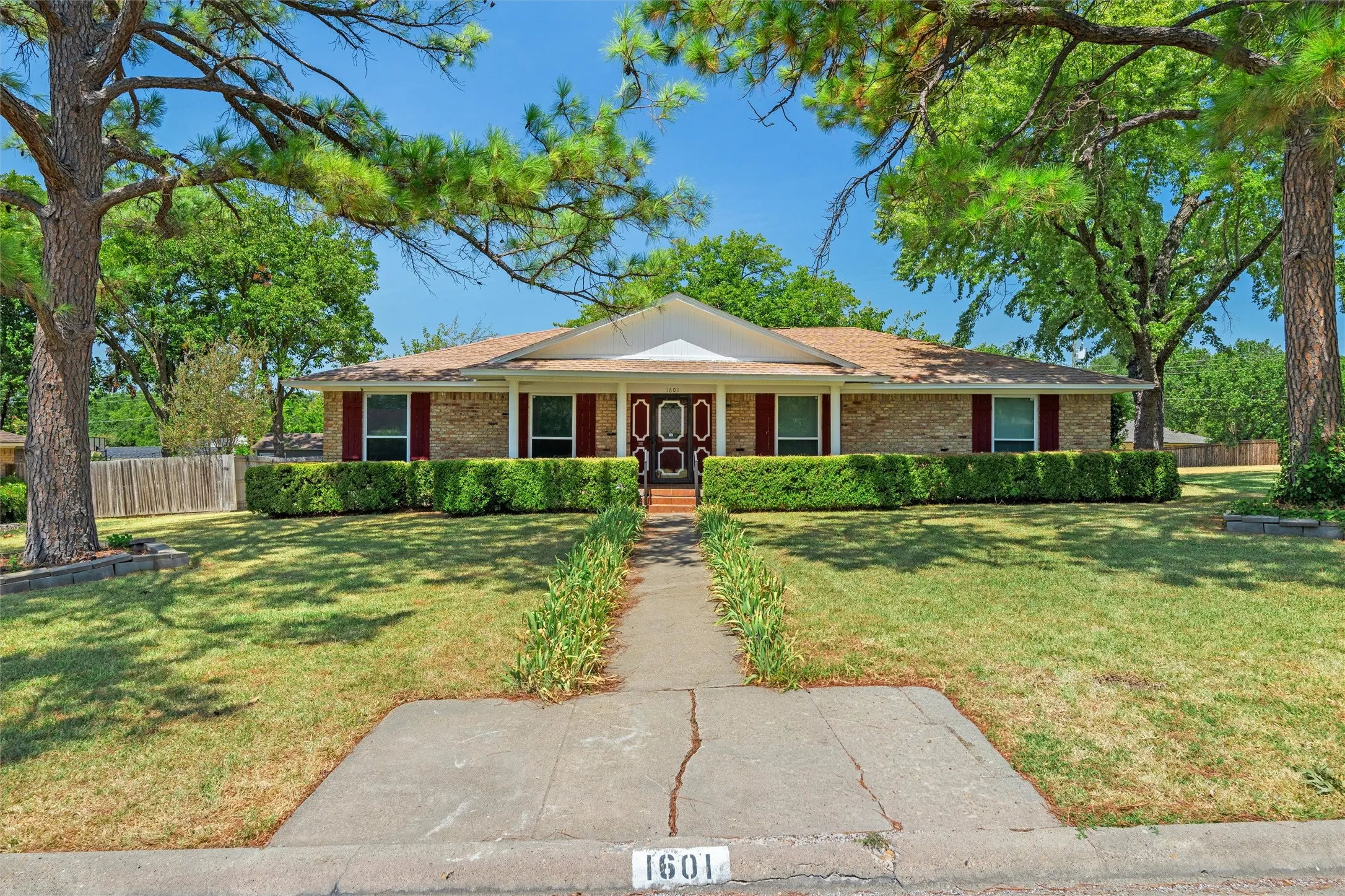 Brick exterior, gabled entry, wood-finish shutters, mature trees, and established landscaping