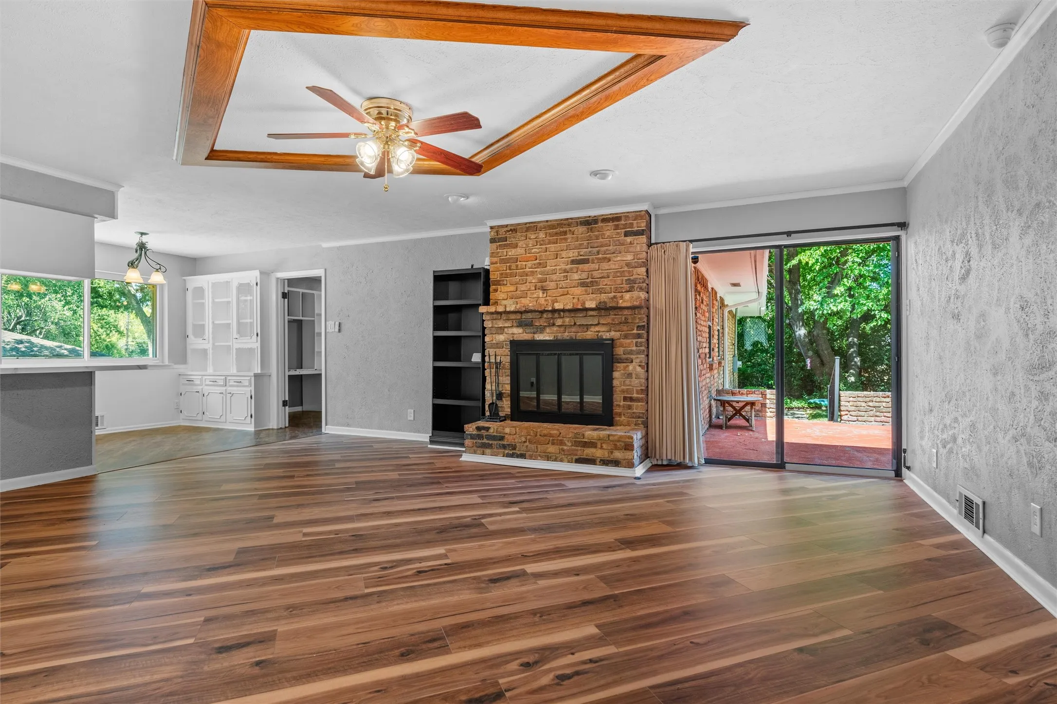 Wood-finish flooring, brick fireplace, wood-coffered ceiling with ceiling fan, built-in shelving, and sliding glass door to exterior