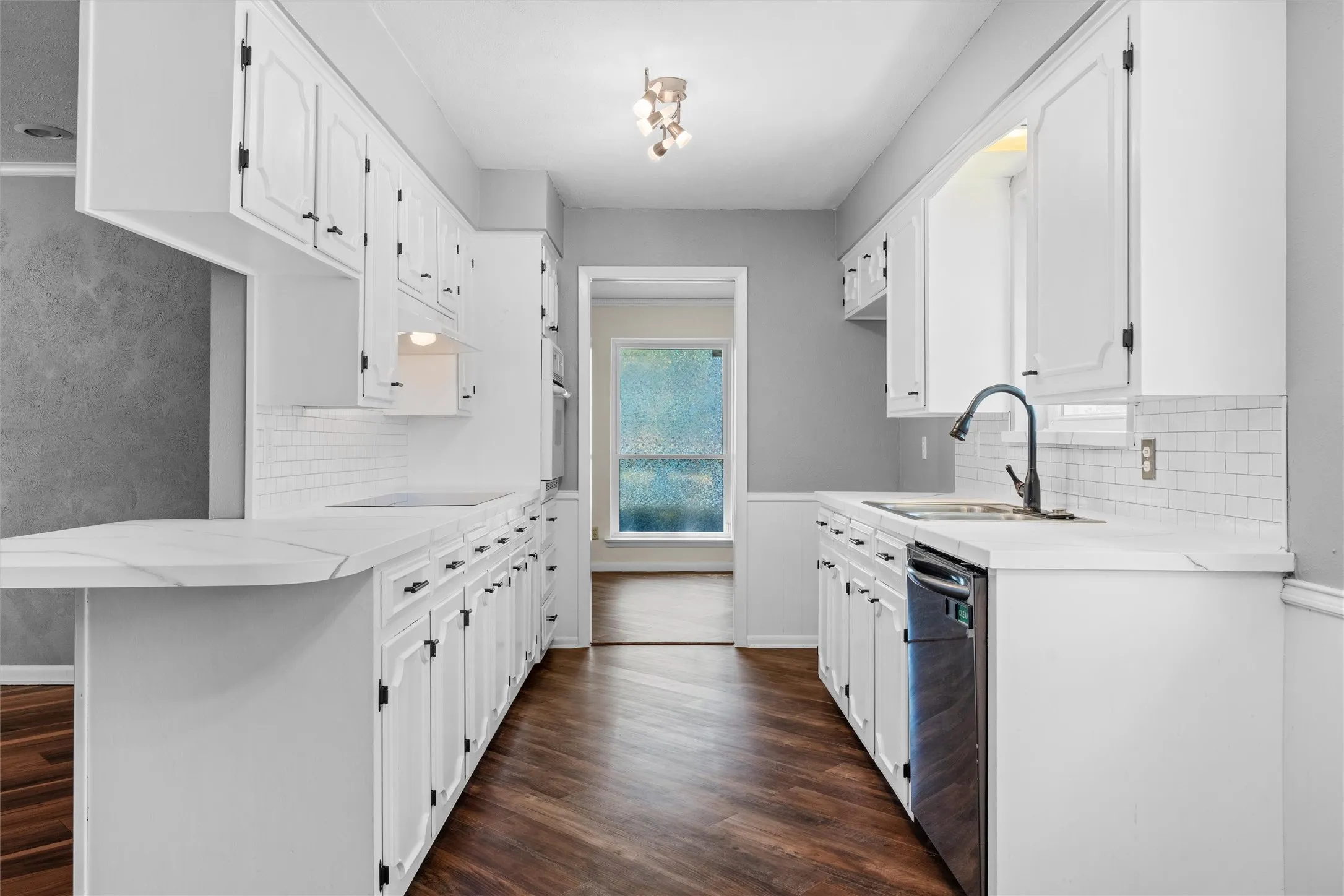 Galley kitchen featuring white cabinetry, light-toned countertops, subway tile backsplash, stainless steel appliances, and wood-finish flooring