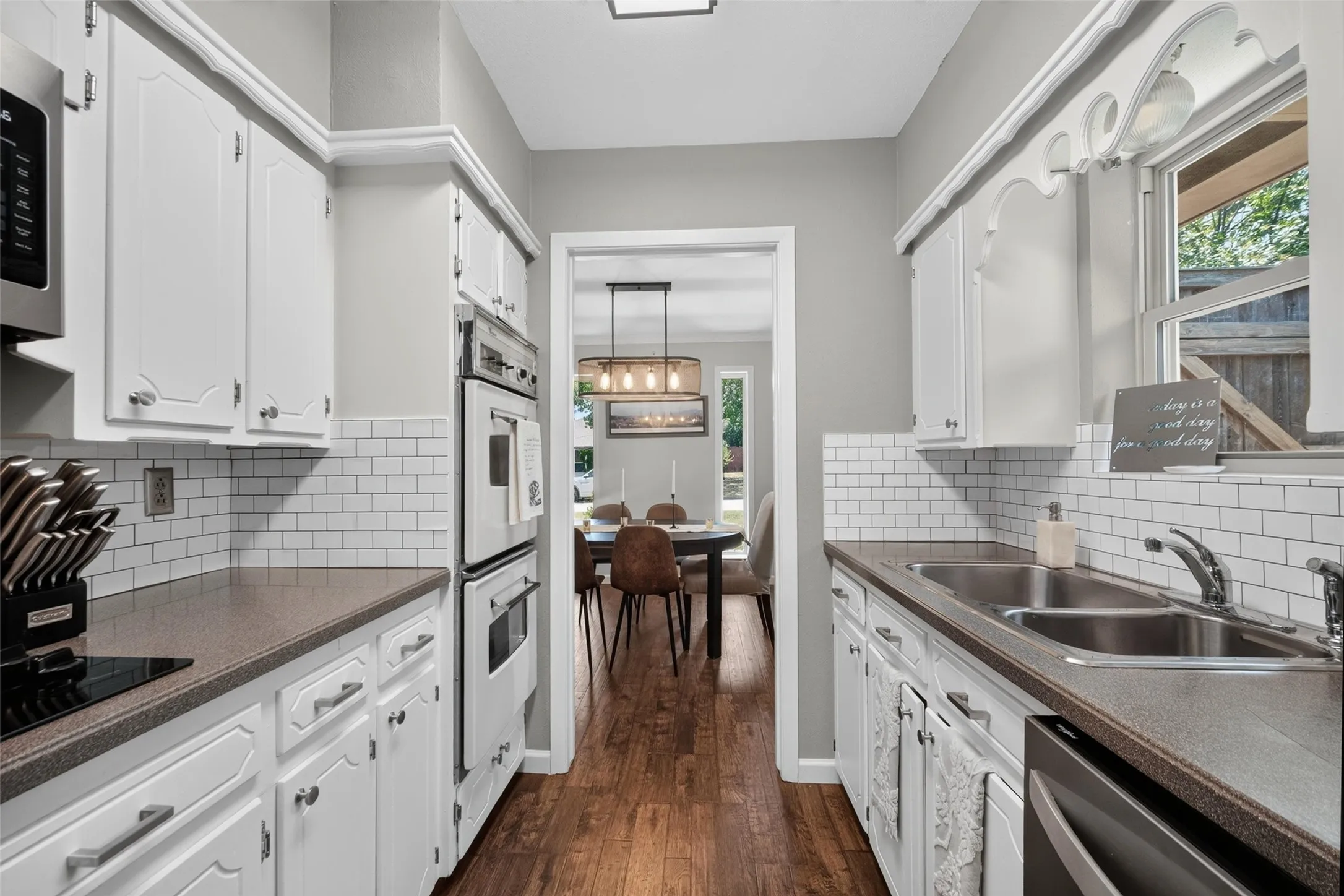 Galley kitchen featuring white cabinetry, subway tile backsplash, built-in double ovens, and wood-finish flooring