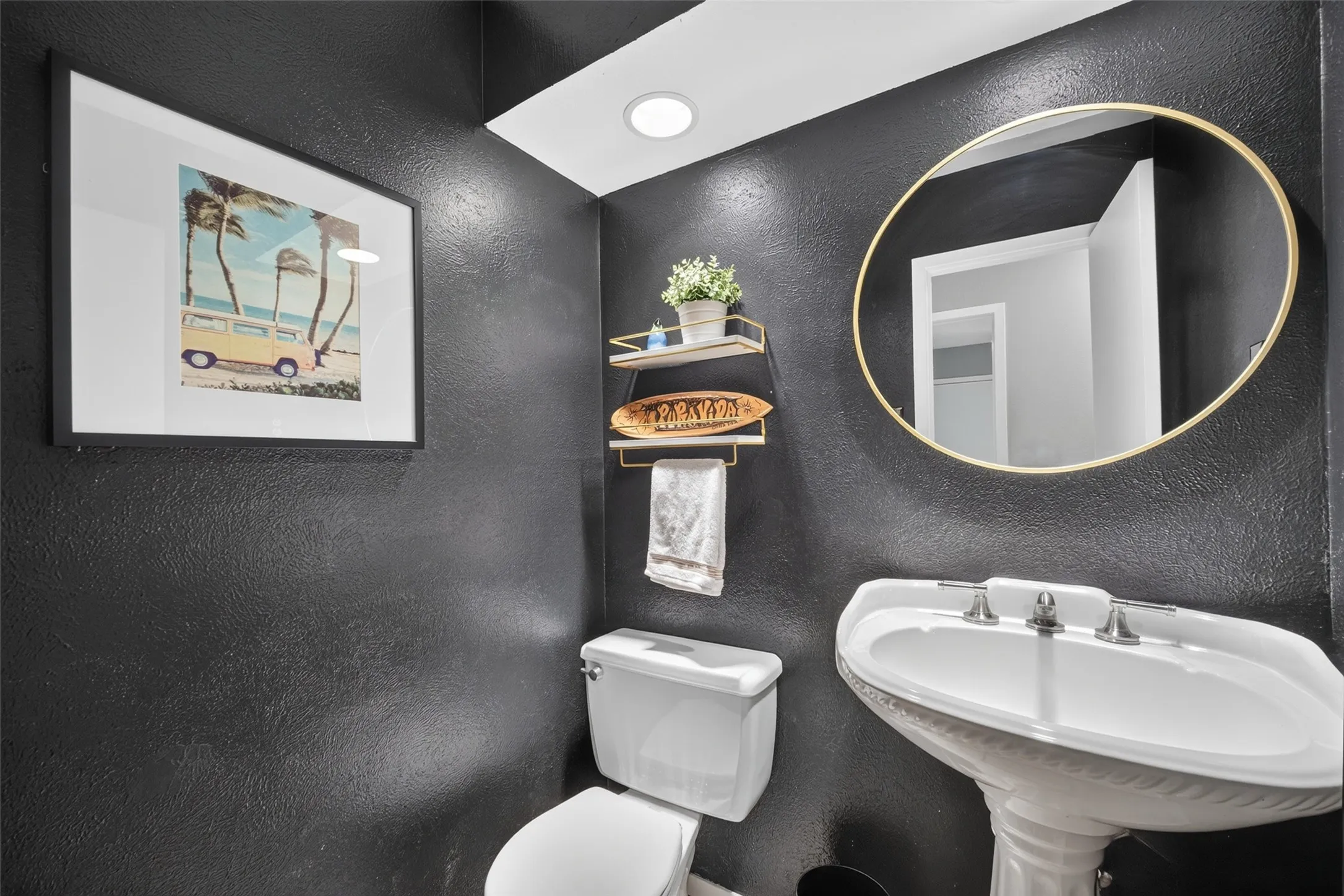 Pedestal sink with three-piece faucet, gold-framed round mirror, and built-in recessed lighting