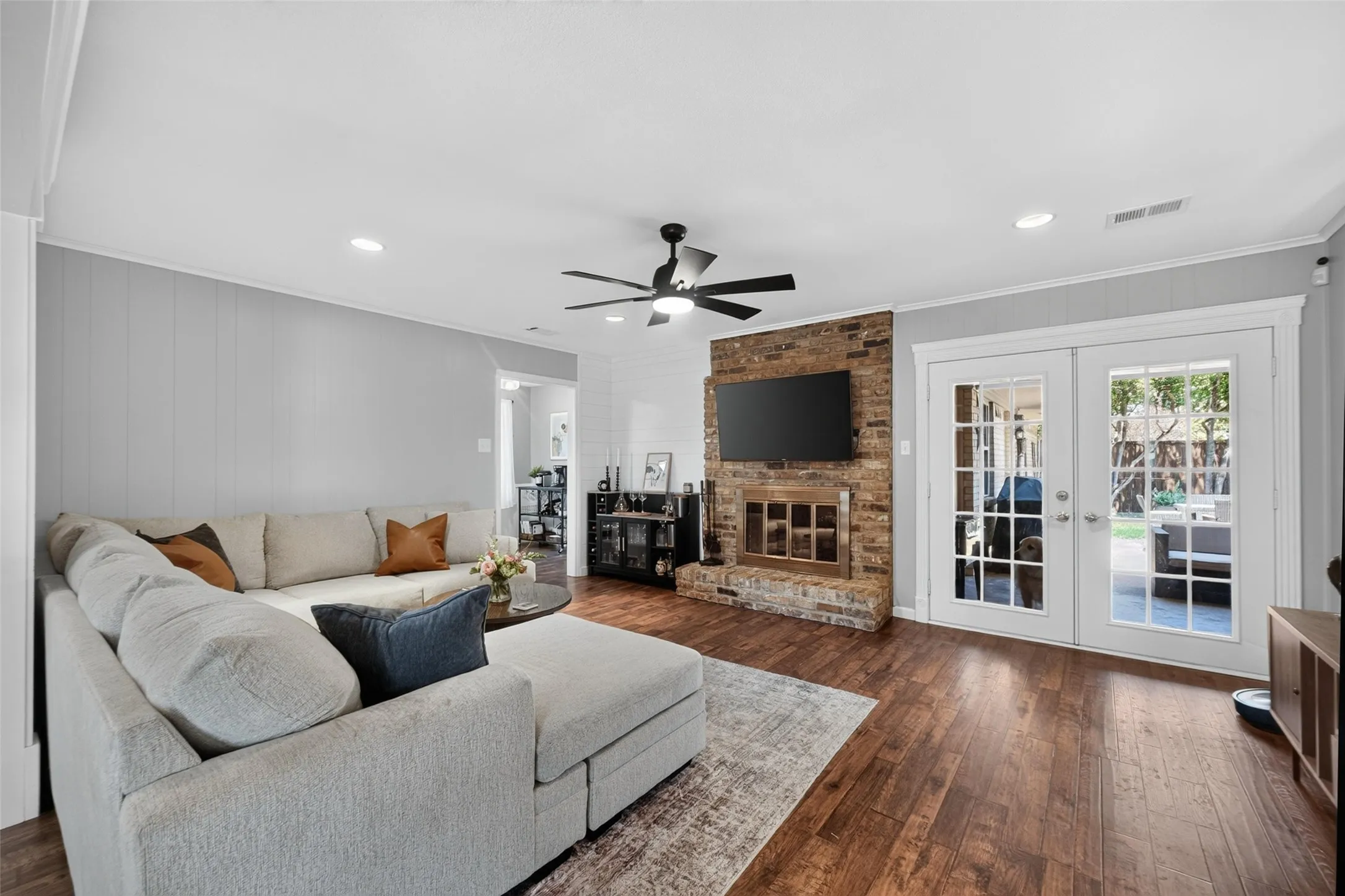 Spacious living area featuring wood-finish flooring, a brick fireplace with a hearth, and built-in recessed lighting