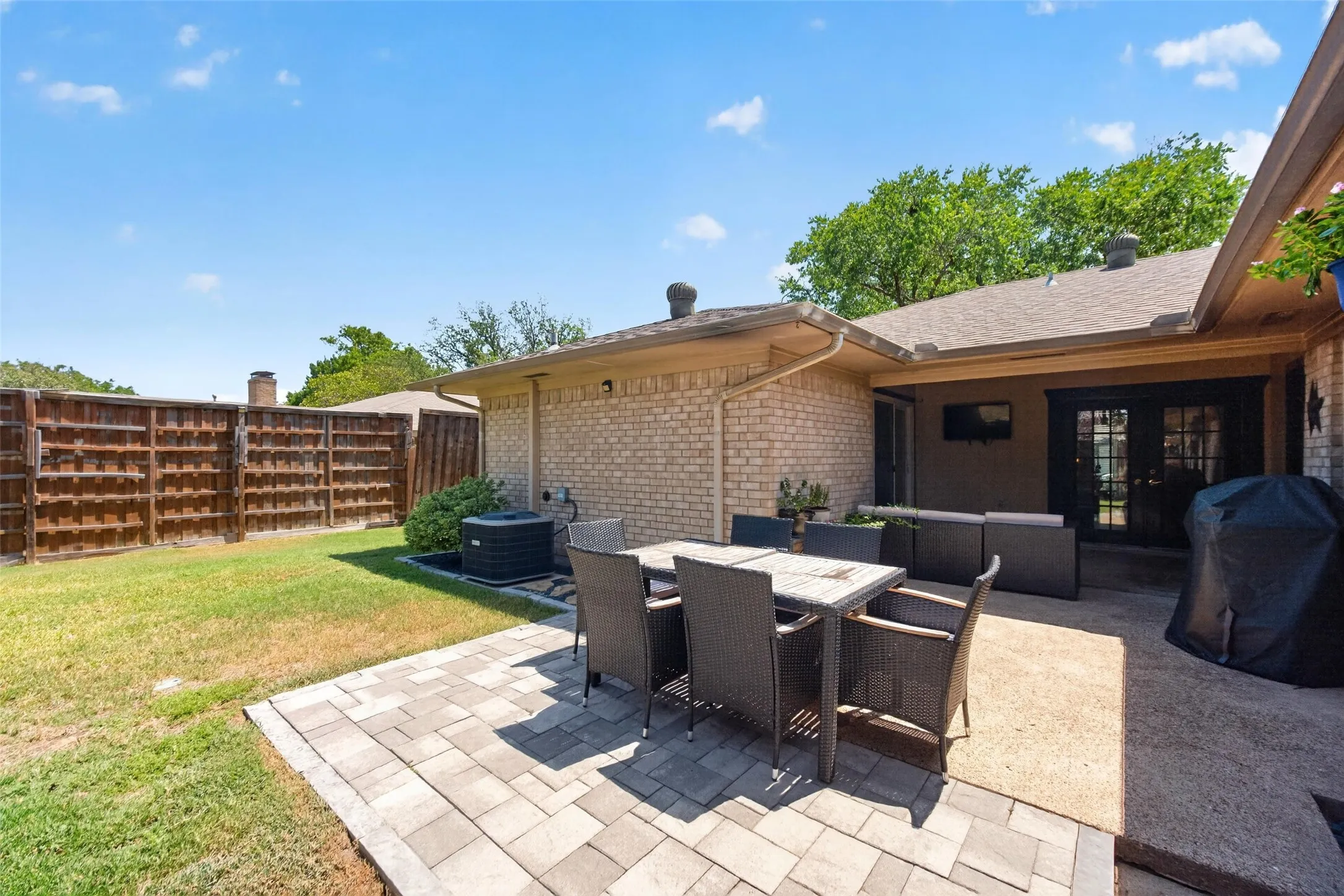 Expansive backyard featuring a manicured lawn, paver patio, brick exterior, and French doors