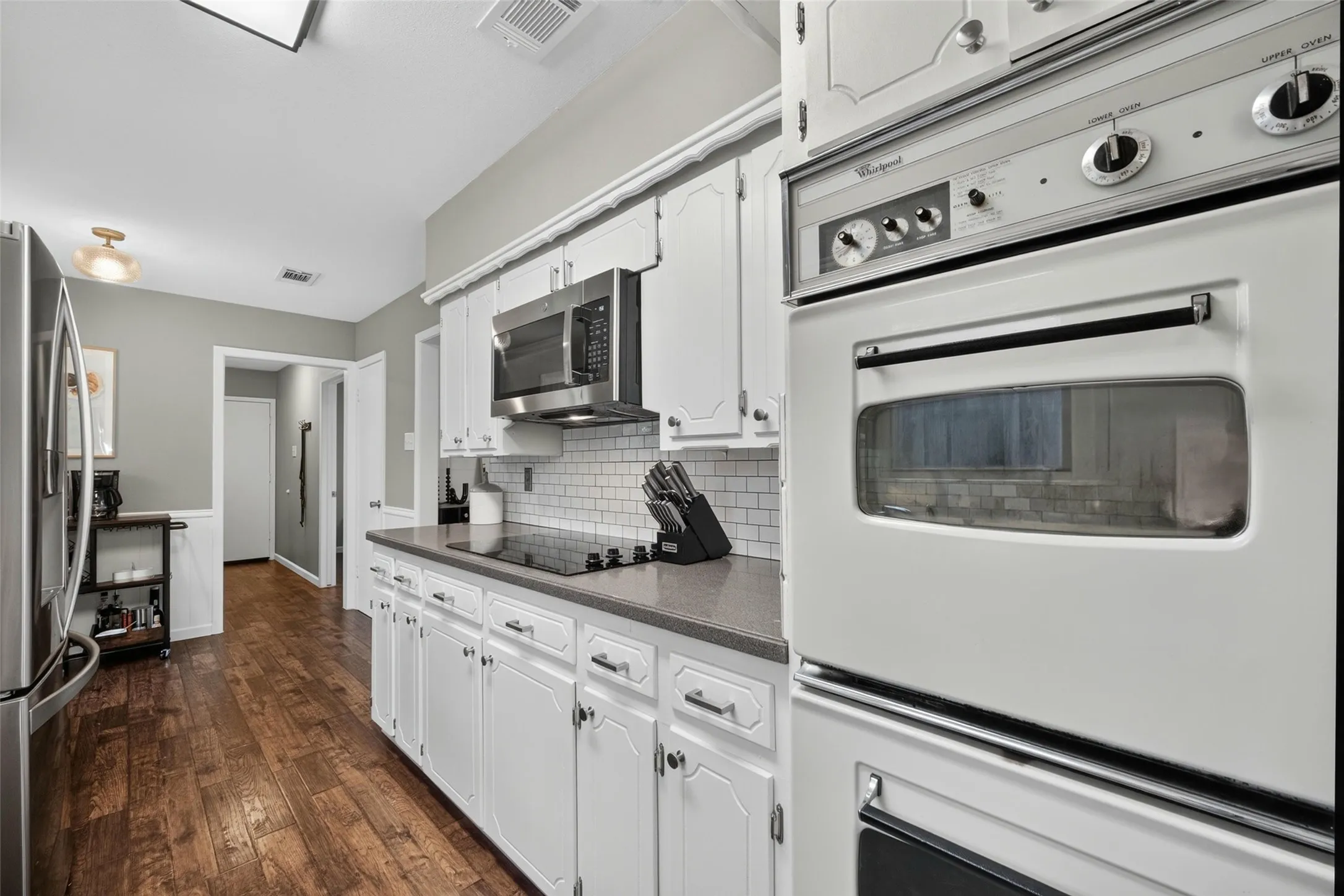 White cabinetry with brushed nickel hardware, durable countertops, stainless steel microwave, integrated cooktop, and built-in double ovens