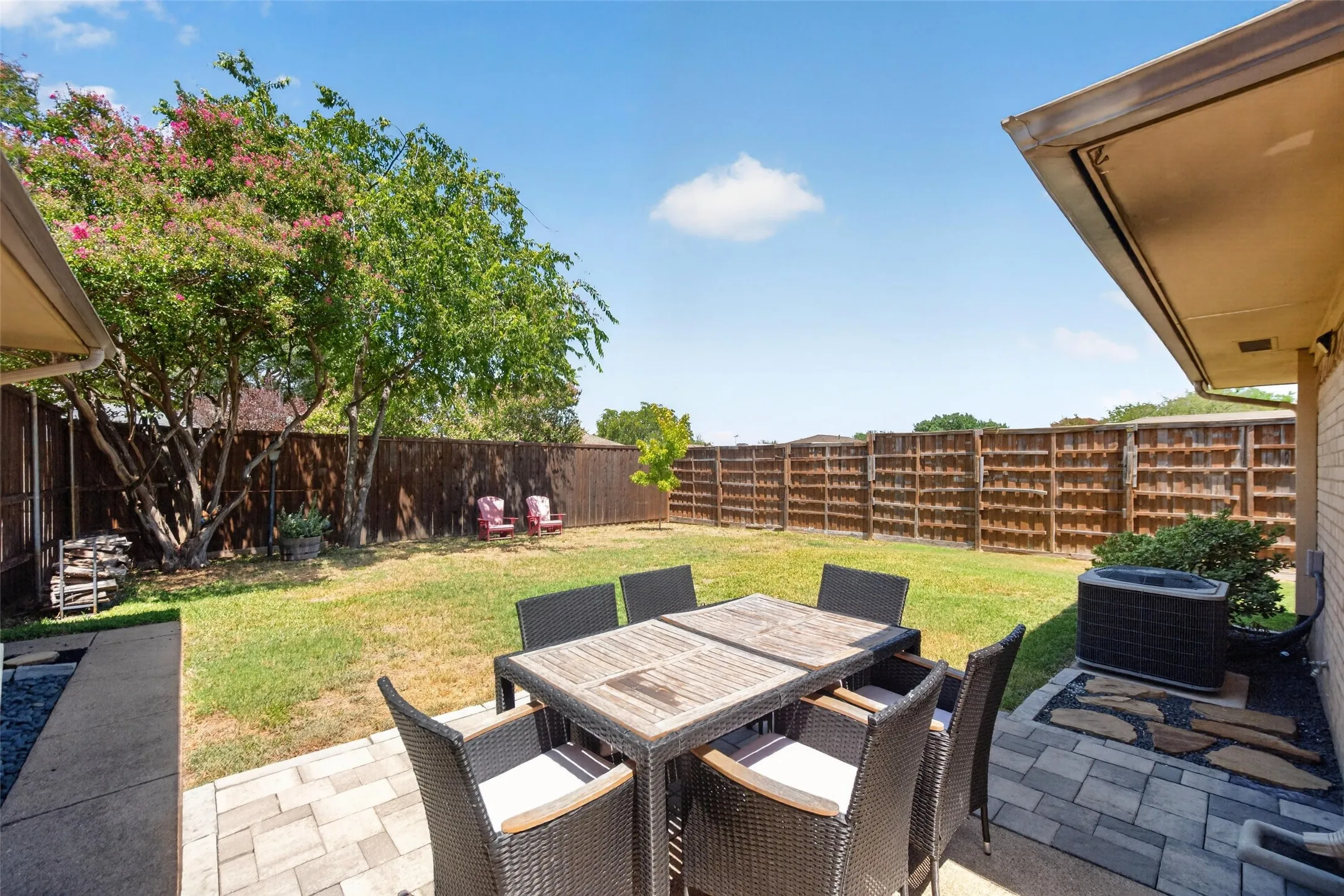 Expansive backyard featuring a wood privacy fence, mature trees, and a paved patio area