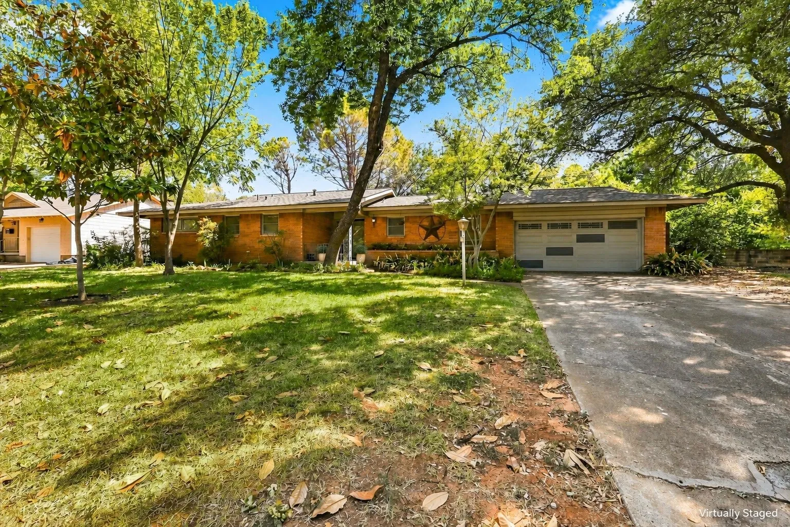 Brick exterior residence featuring a front lawn with mature trees, an attached garage, and a paved driveway