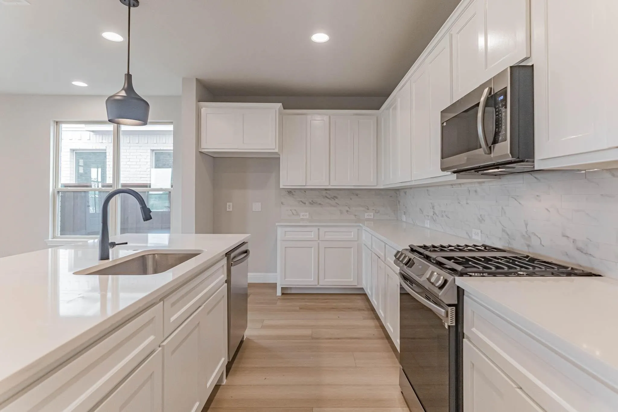 White shaker cabinetry, light-toned wood-finish flooring, stainless steel appliances, quartz countertops, and a full-height backsplash